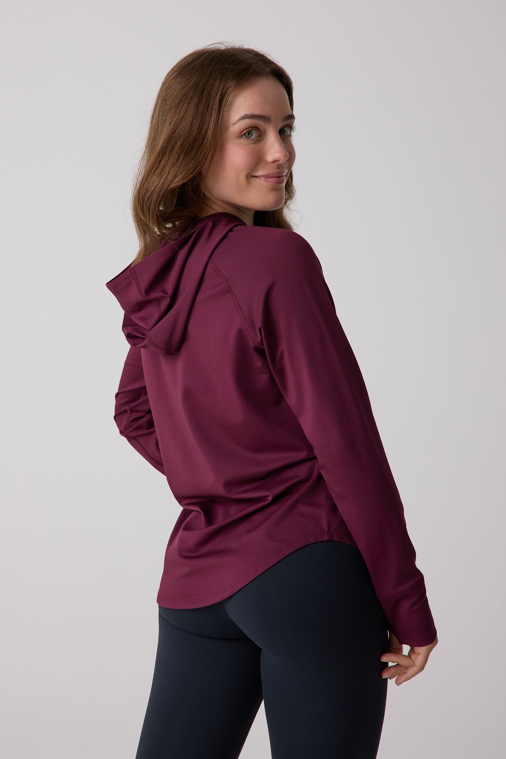 Maroon long-sleeve women's layering hoodie by Centerline Athletics, worn by a woman smiling over her shoulder with black leggings.
