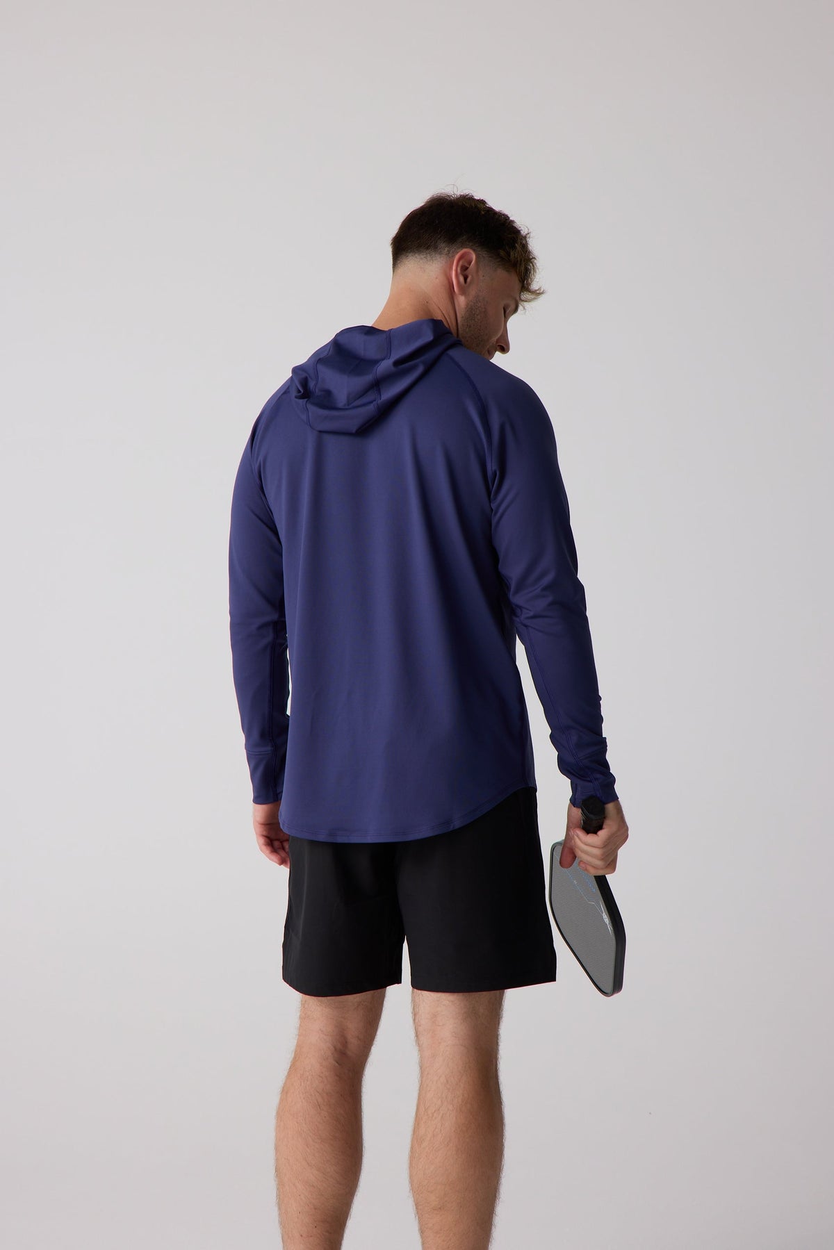 Navy blue men's layering hoodie with raglan sleeves and curved hem, shown from back view on model wearing black shorts holding a paddle.