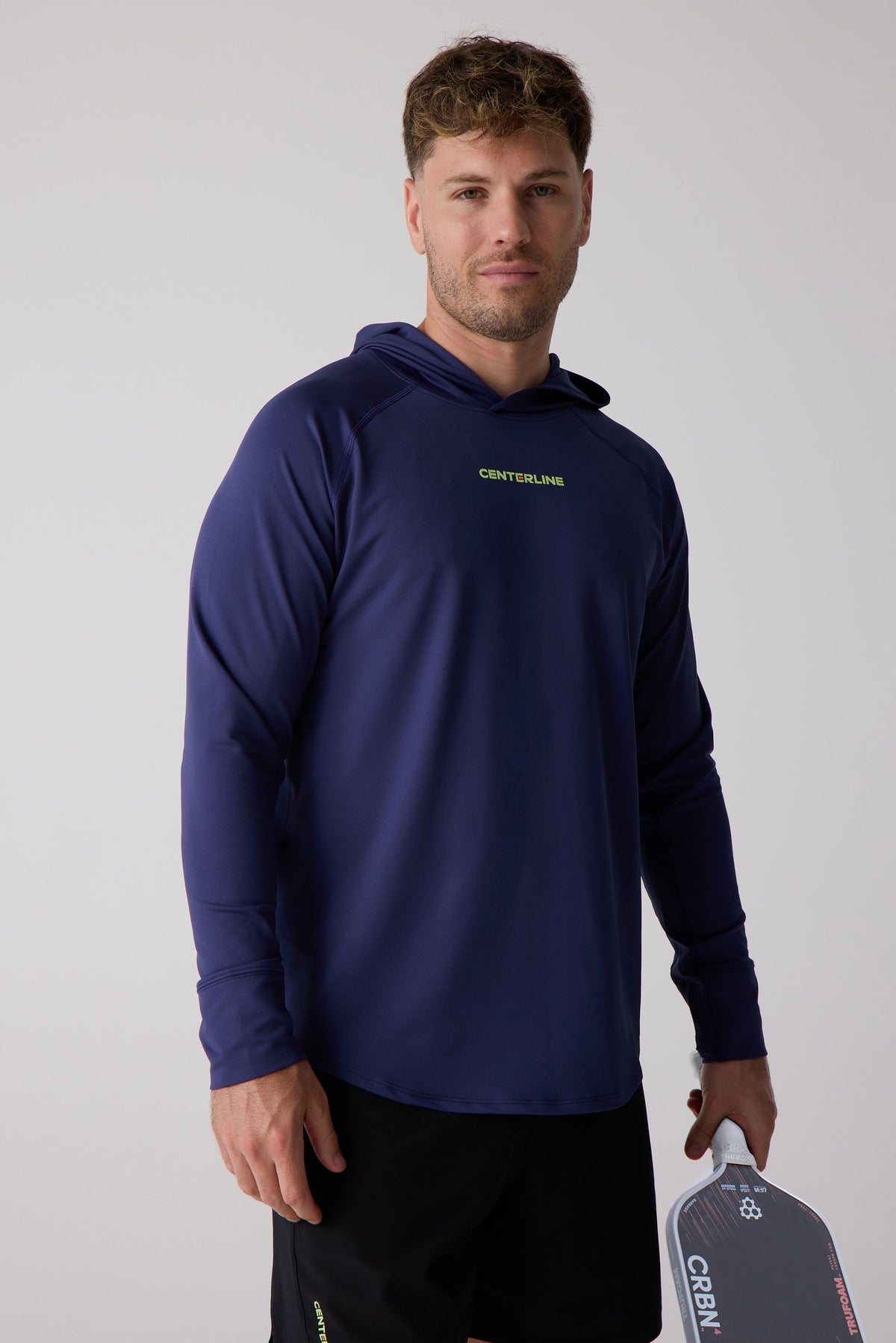 Navy blue men's layering hoodie by Centerline with lime green logo, ribbed cuffs, and hood, worn in lifestyle front view with paddle.
