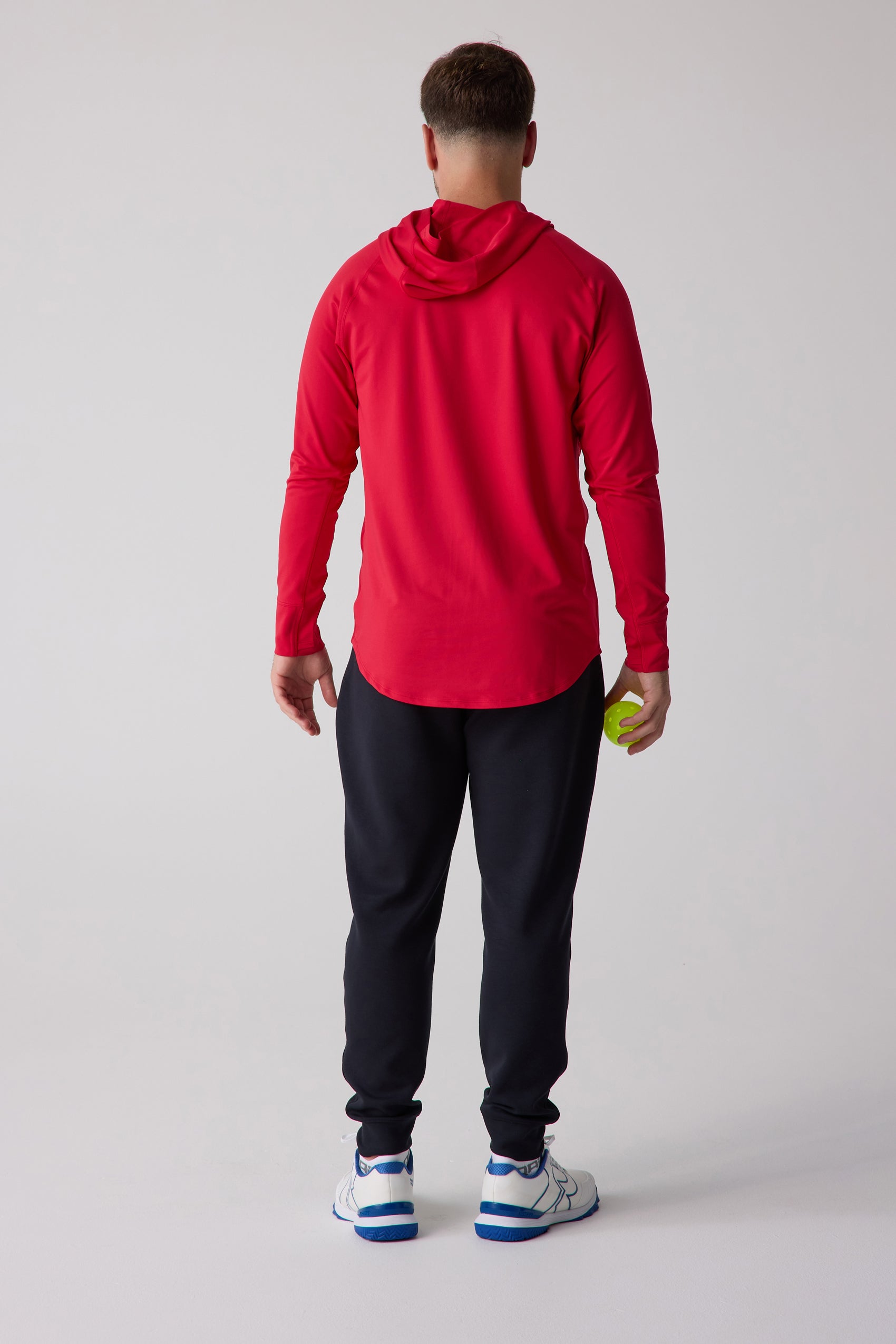 Red men's layering hoodie by Centerline Athletics, shown from the back with black sweatpants and athletic shoes, holding a yellow pickleball.