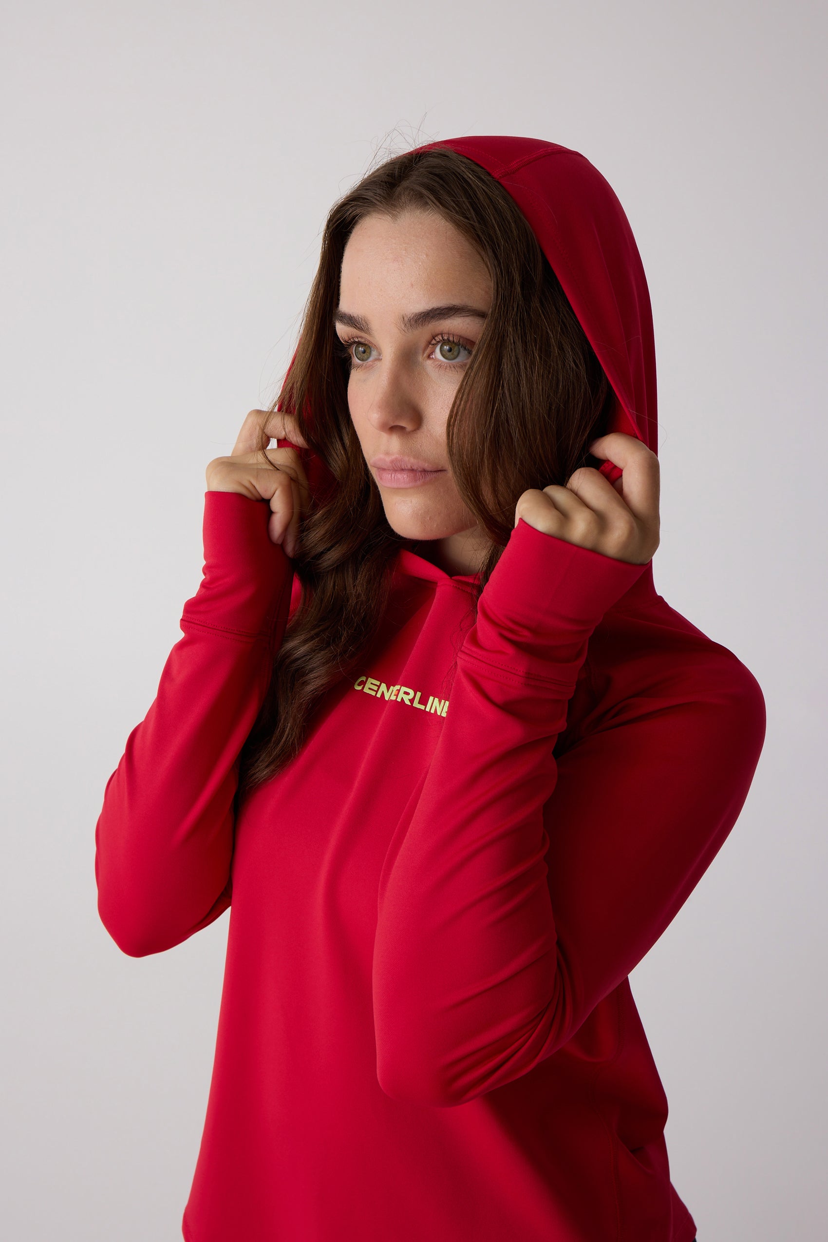 Red women's layering hoodie by Centerline Athletics, worn by a model adjusting the hood, showing a yellow chest logo.