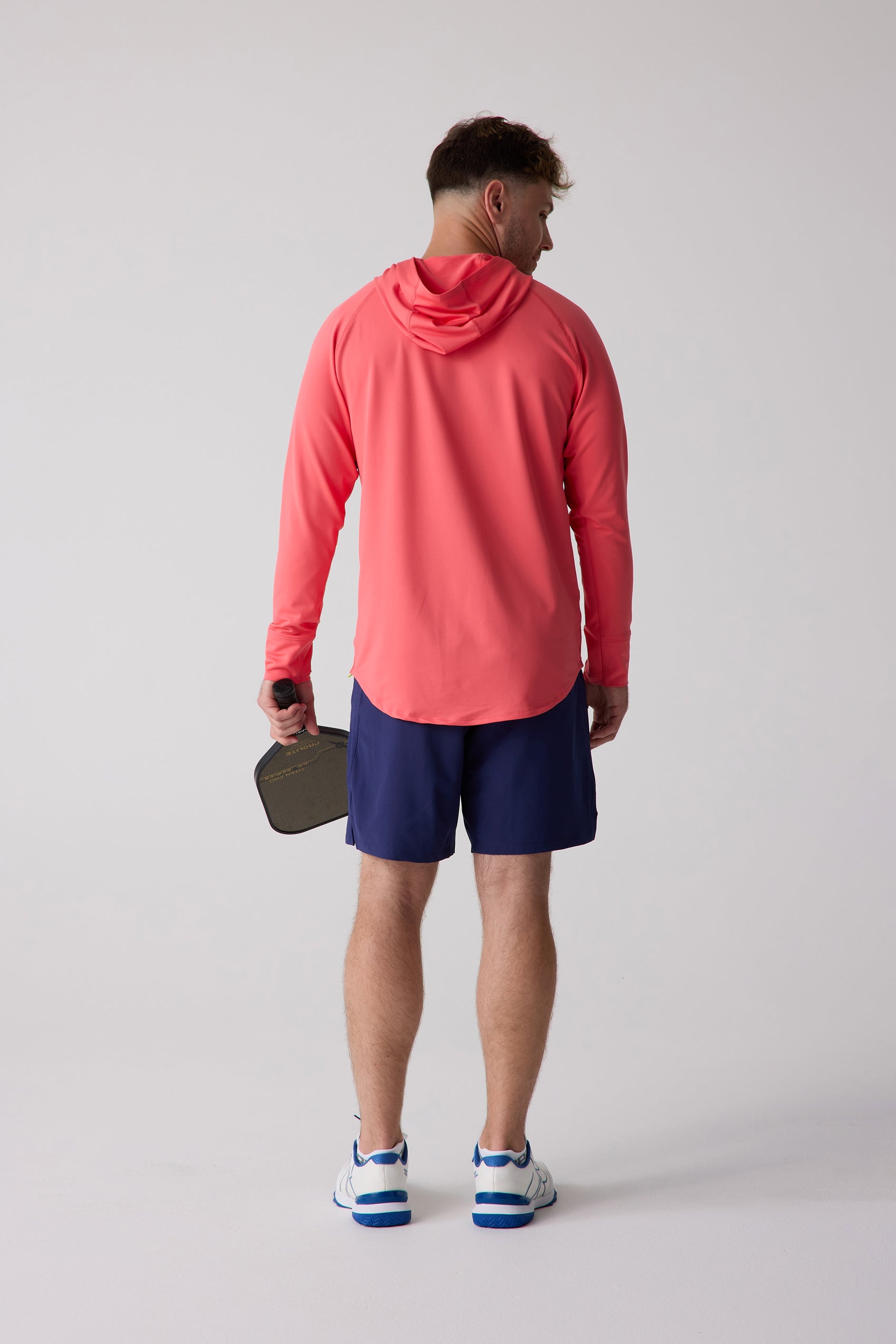 Coral Men's Layering Hoodie by Centerline Athletics, back view on a man wearing navy shorts and white and blue shoes, holding a pickleball paddle.