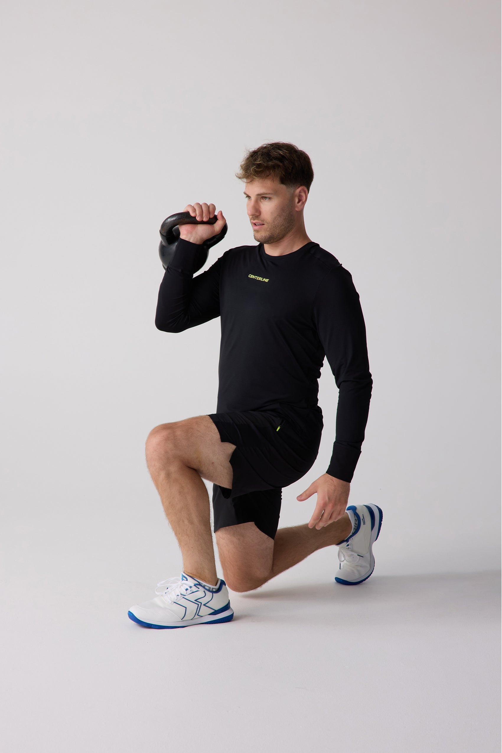 Black Men's AirLite Long Sleeve by Centerline Athletics, featuring yellow "CENTERLINE" text, on a man performing a kettlebell lunge.