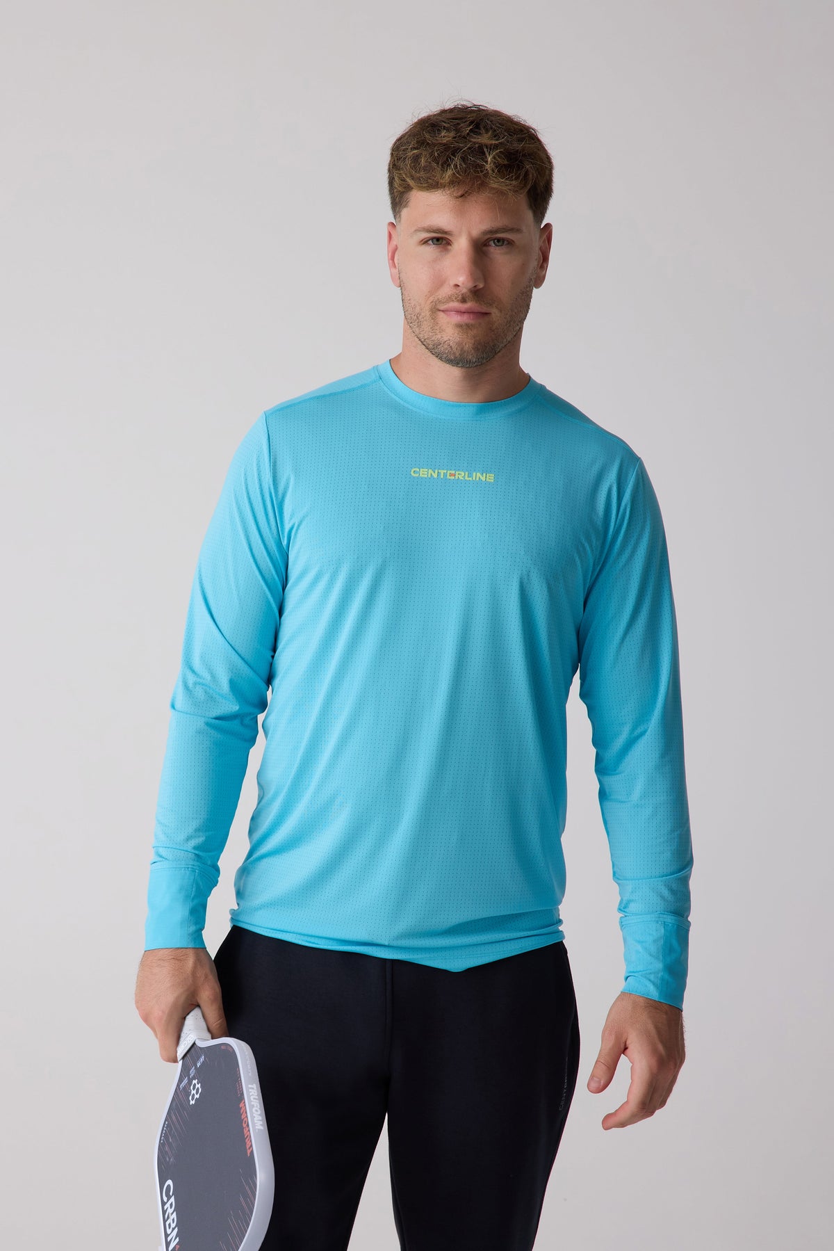 Turquoise men's long sleeve performance shirt with mesh texture and chest logo, worn by model holding paddle, front view