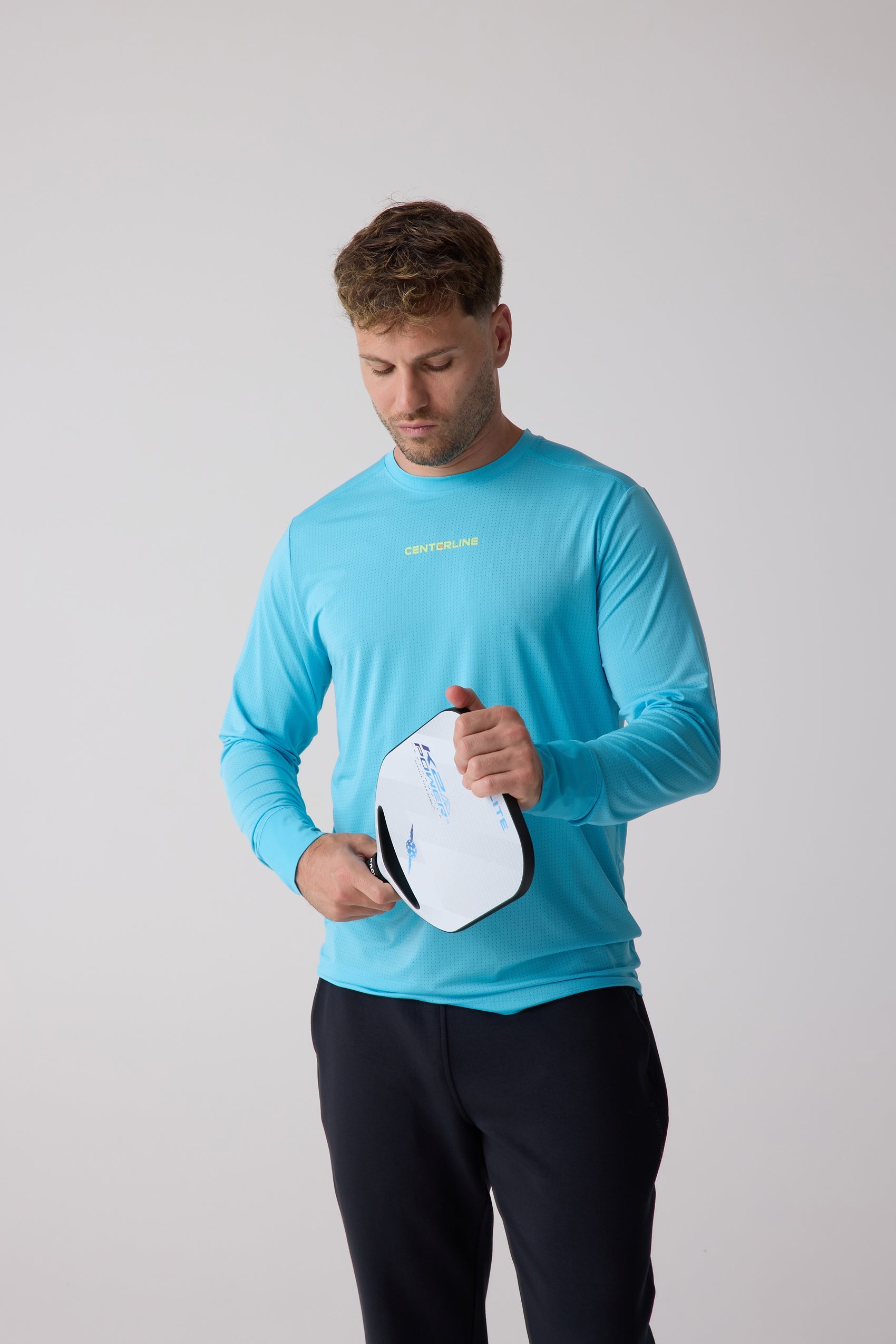 Blue perforated Men's AirLite Long Sleeve by Centerline Athletics, with brand text on chest, worn by a man holding a pickleball paddle.