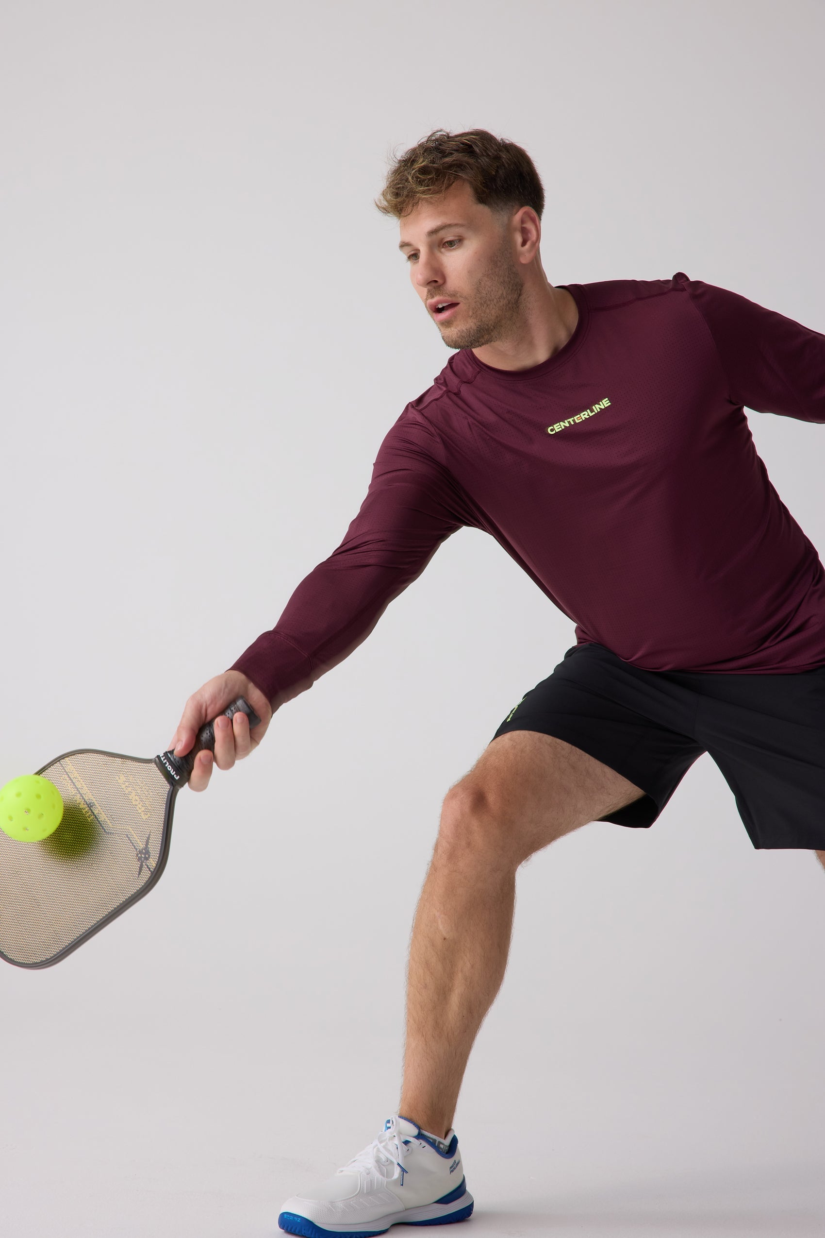 Maroon long sleeve shirt by Centerline Athletics with a neon yellow logo and subtle perforated texture, worn by a man playing pickleball.
