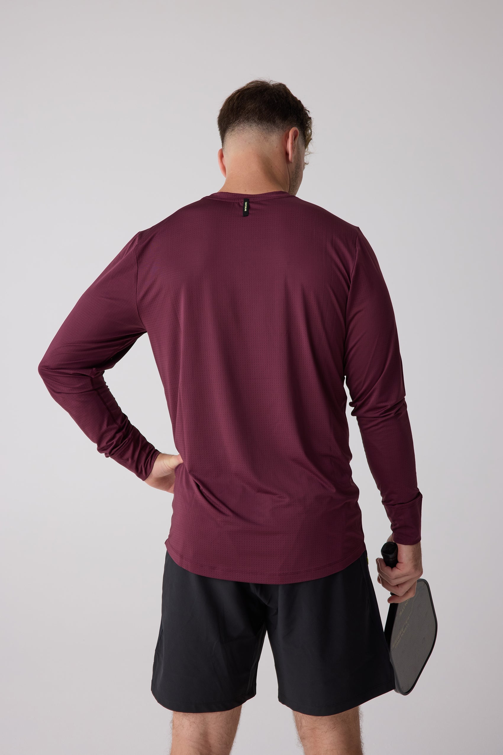 Maroon mesh long sleeve shirt by Centerline Athletics, back view worn by a man in black shorts holding a pickleball paddle.