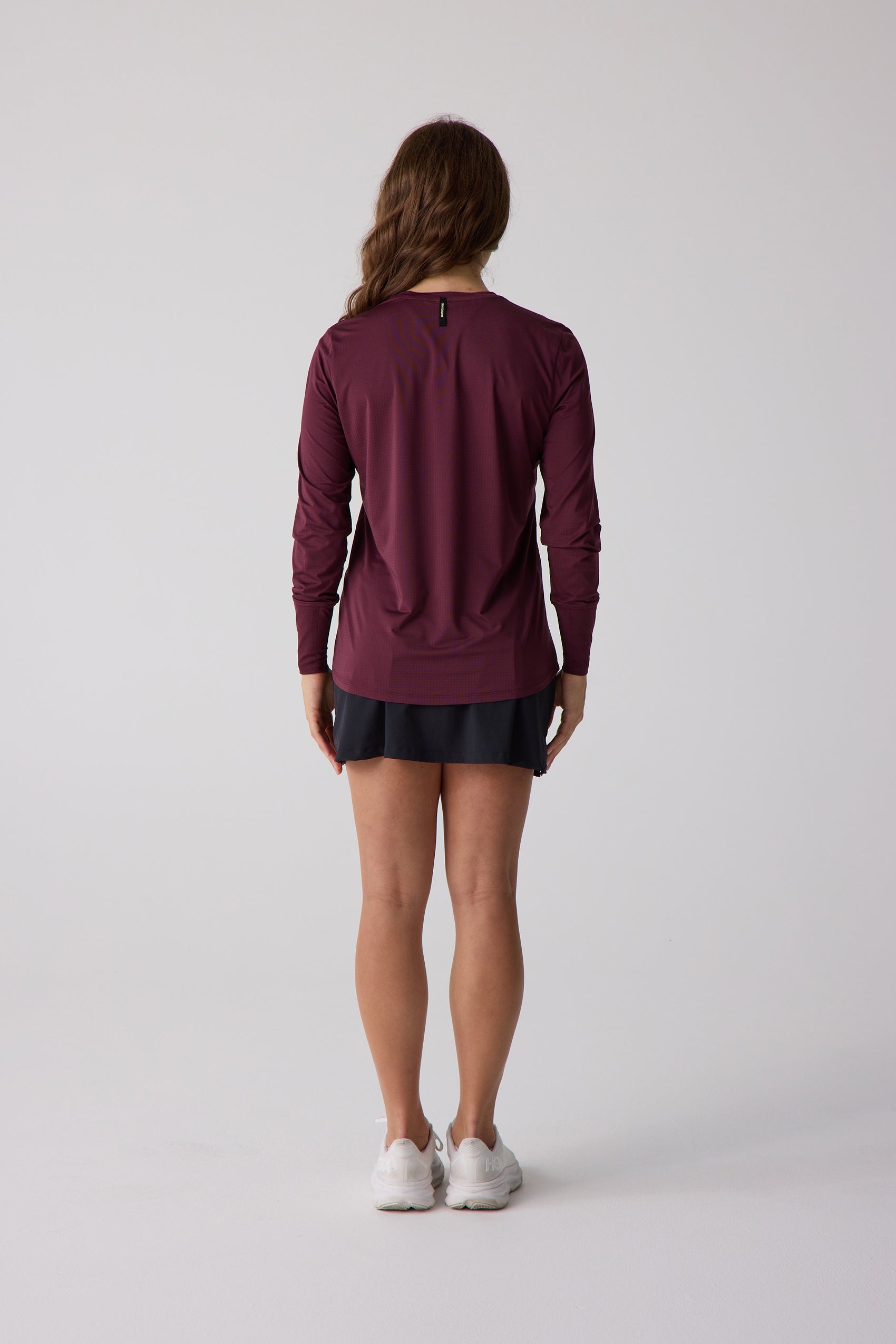 Maroon women's long sleeve shirt by Centerline Athletics with a subtle pattern, styled with a black skirt and white sneakers, back view.