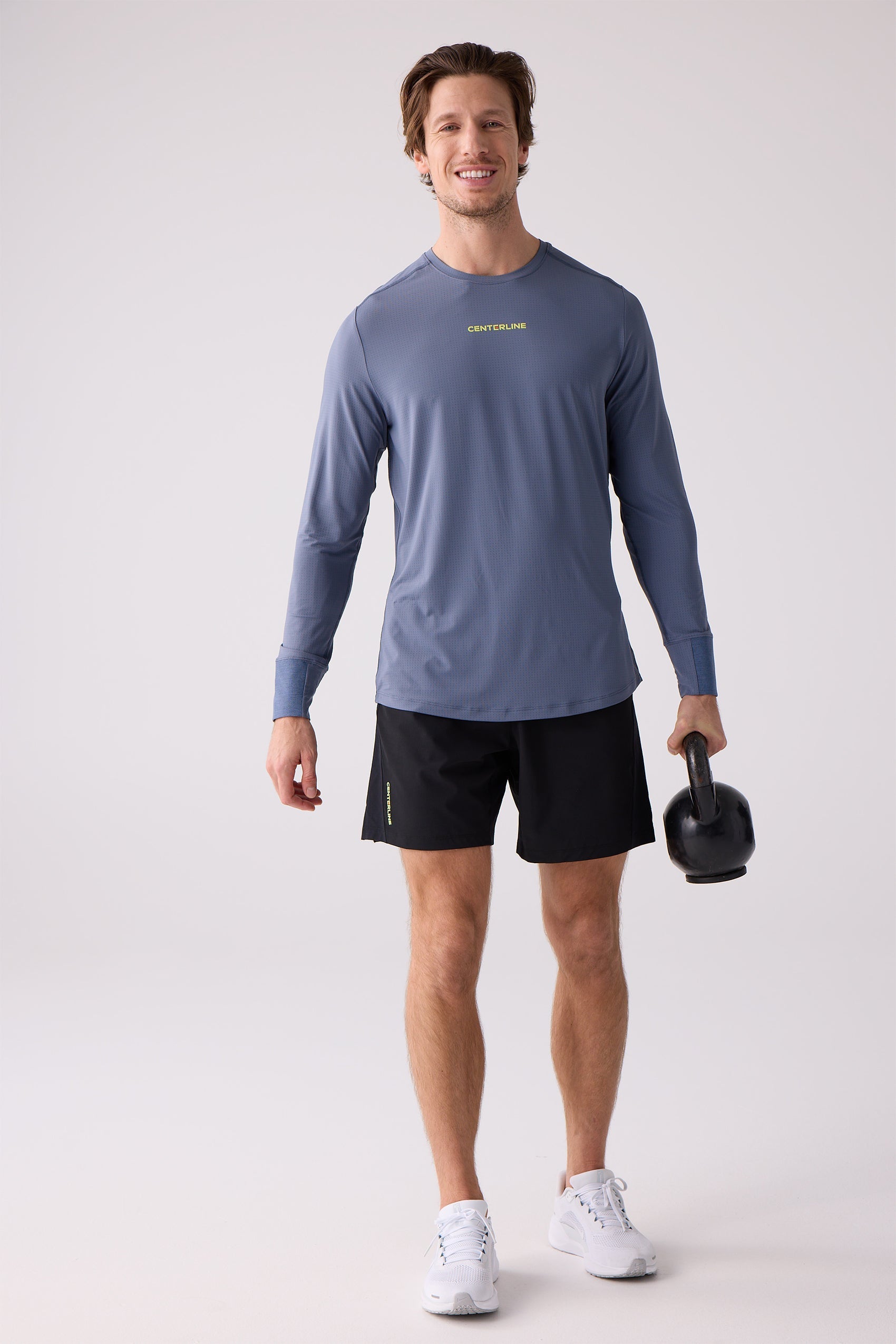 Men's slate blue AirLite long sleeve shirt by Centerline Athletics, featuring a subtle perforated texture, yellow chest logo, and extended cuffs, worn by a man with black shorts.