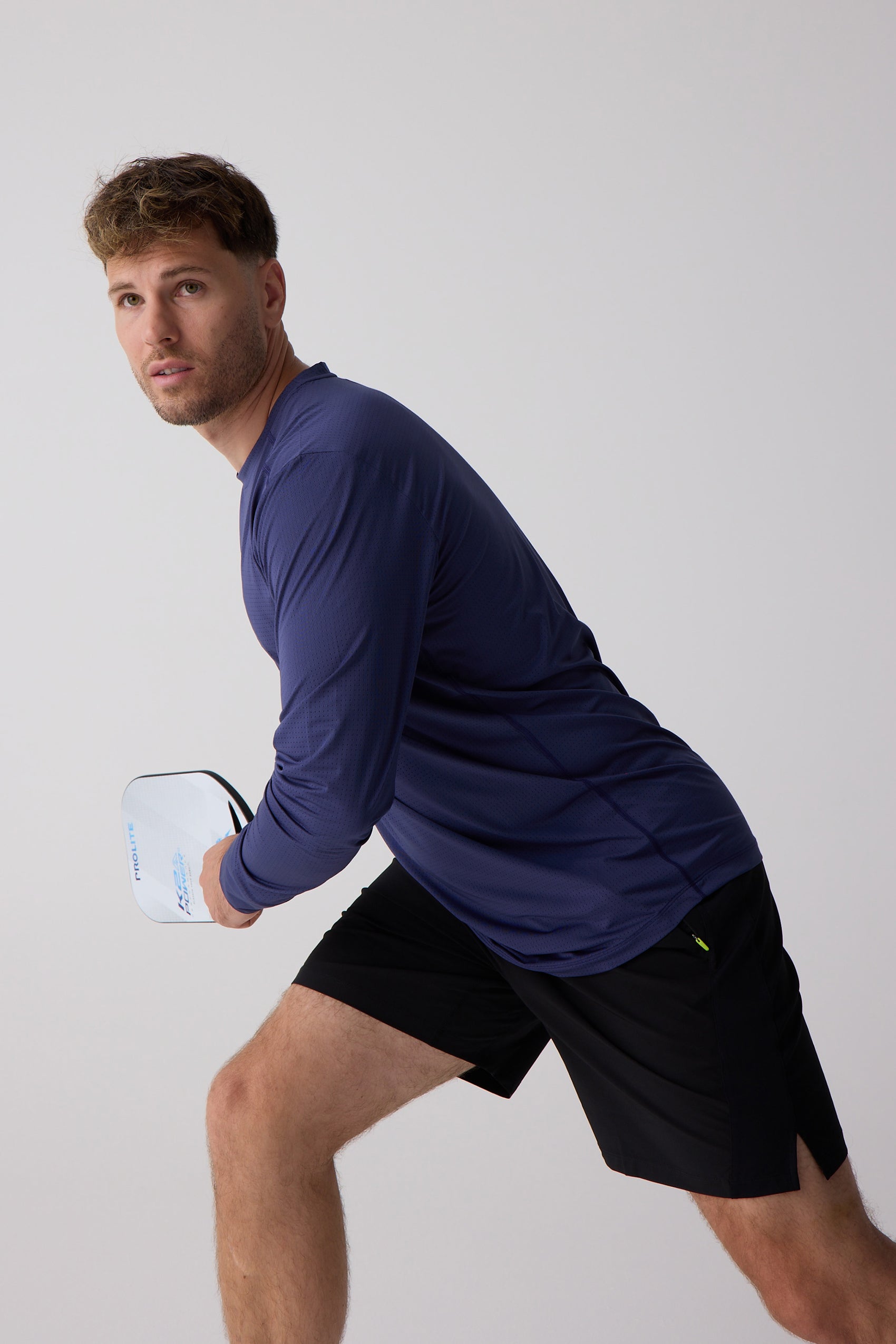 Navy blue perforated Men's Long Sleeve Shirt by Centerline Athletics, worn by a man holding a white PROLITE pickleball paddle.