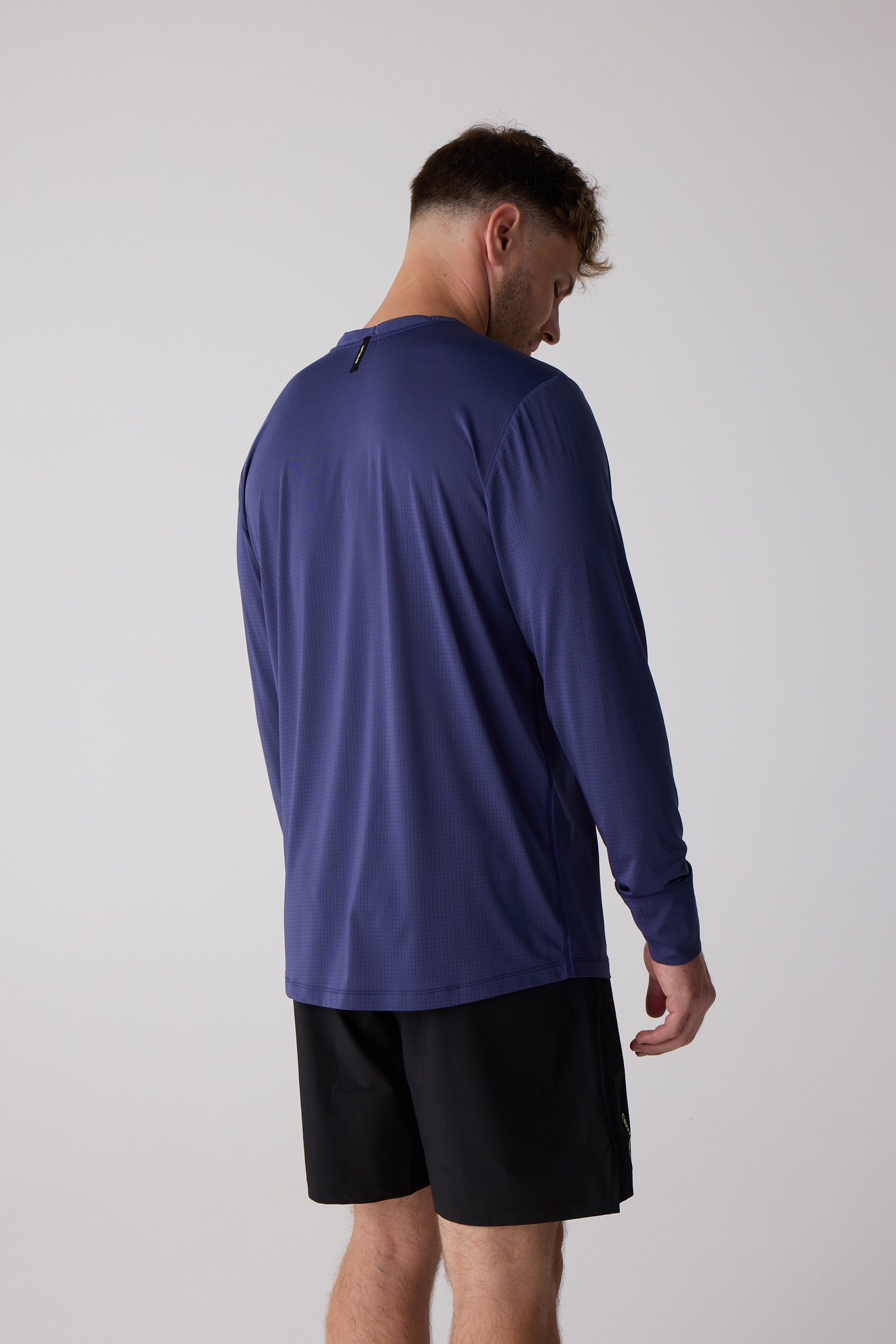 Deep blue long sleeve shirt by Centerline Athletics with micro-dot fabric and a neck tag, worn from the back by a man in black shorts.
