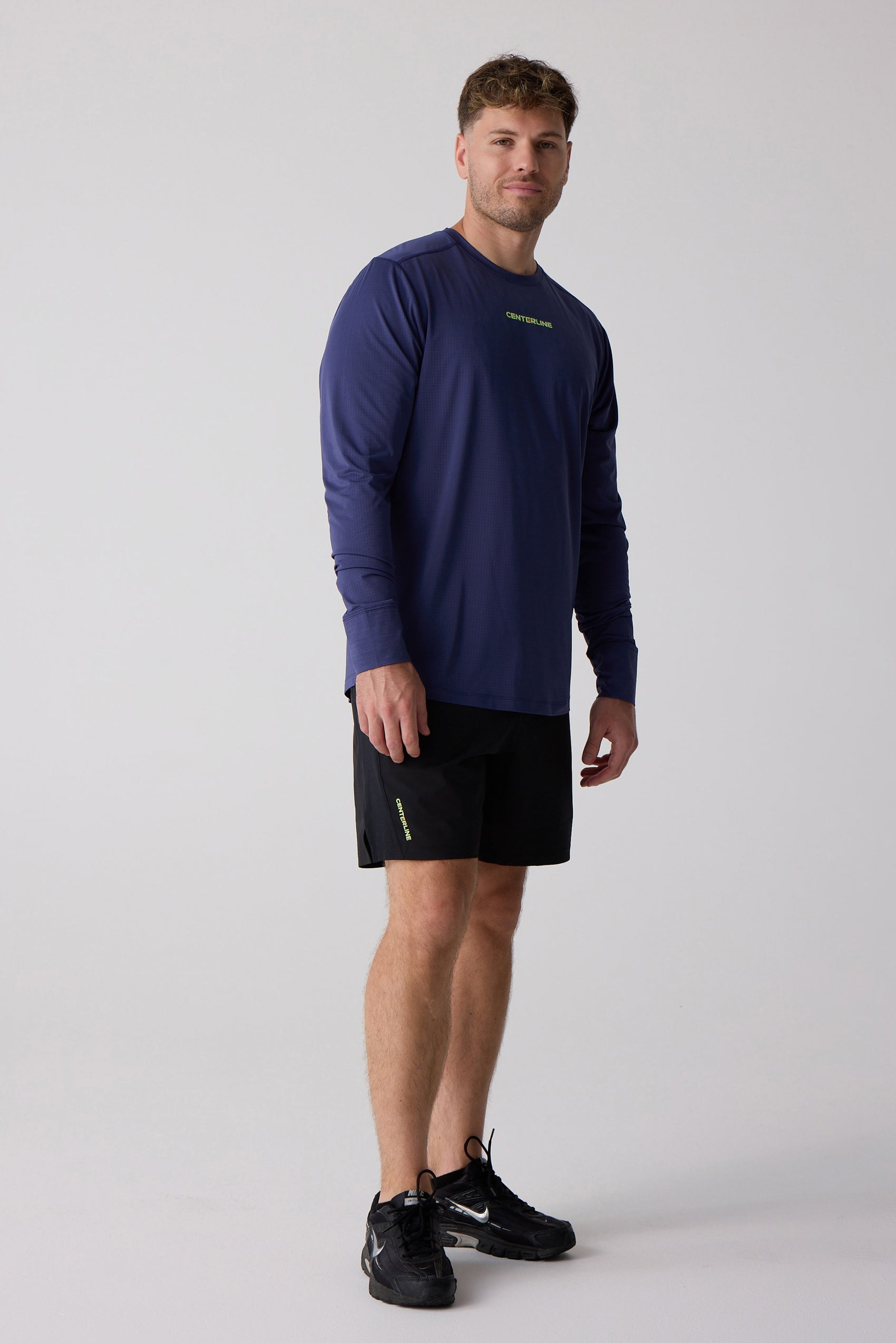 Navy blue men's long sleeve shirt by Centerline Athletics, with textured fabric and neon green chest logo, worn with black shorts and black sneakers.