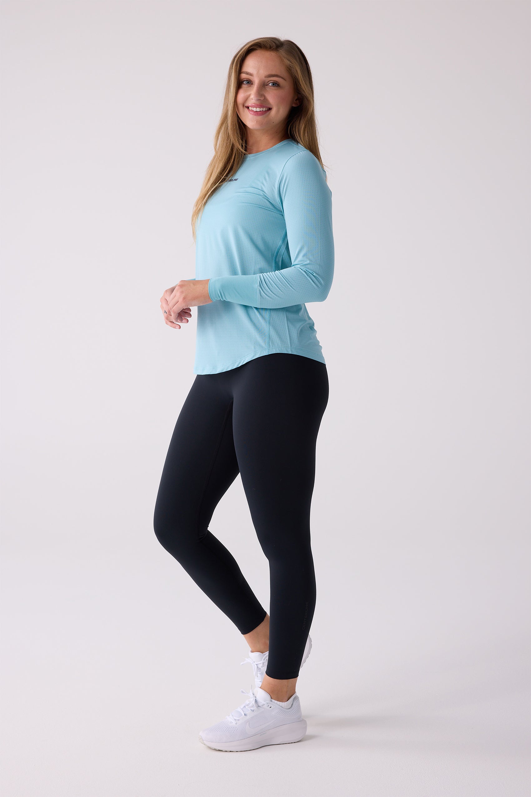 Light blue women's long sleeve shirt by Centerline Athletics with a subtle perforated texture, worn by a model with black leggings and white sneakers.