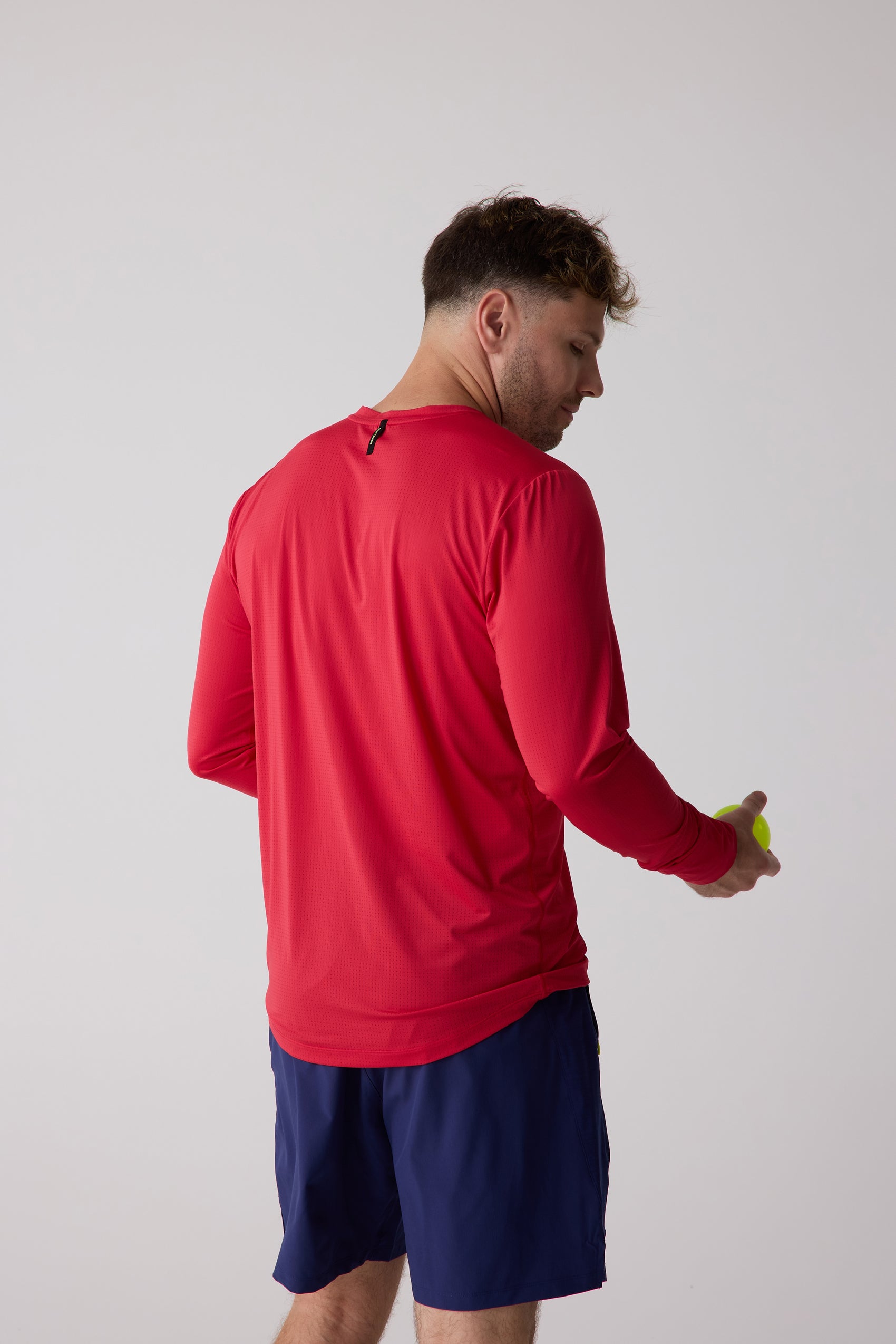 Red men's long sleeve shirt with perforated texture by Centerline Athletics, viewed from the back, worn with navy shorts.