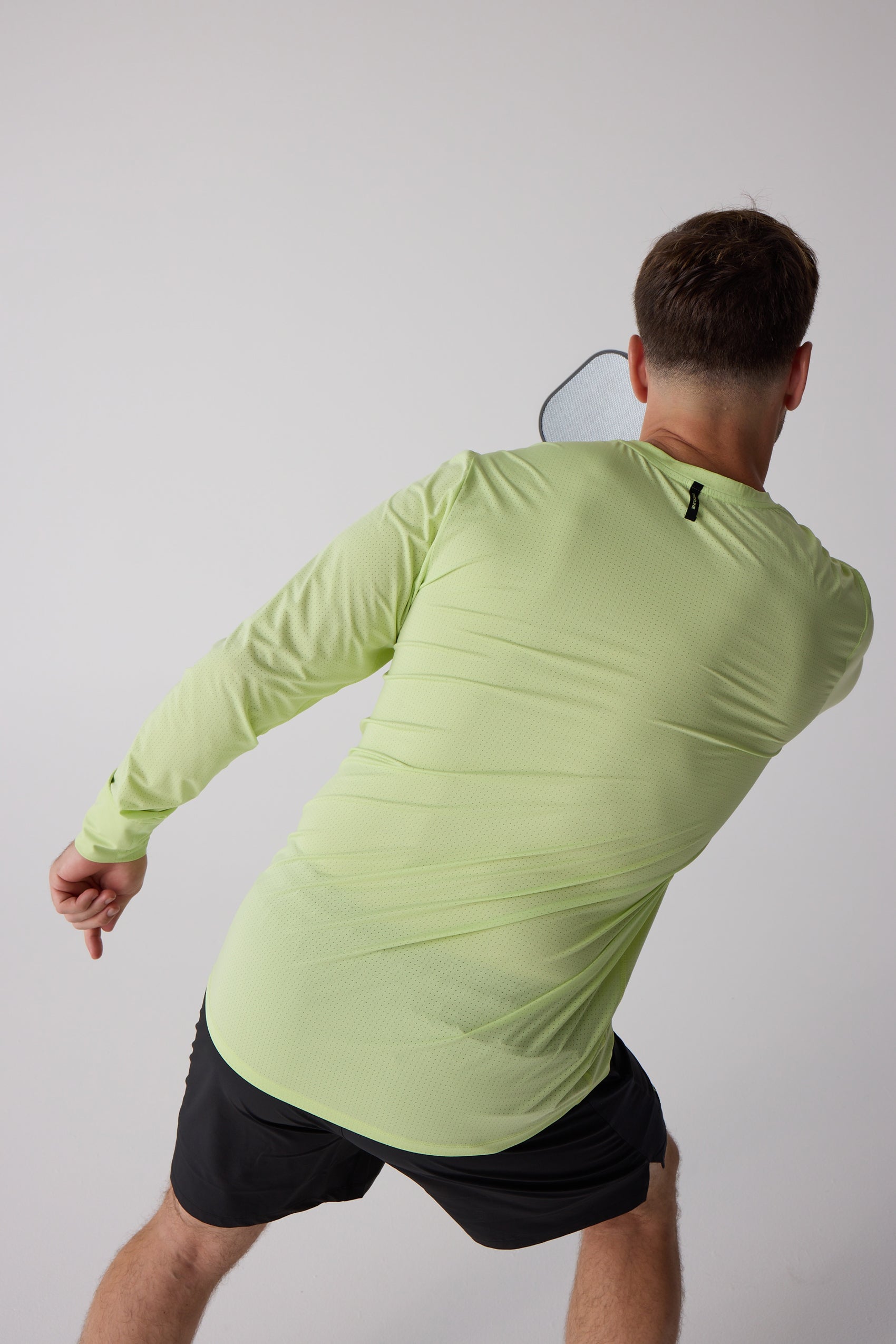 Men's lime green AirLite long sleeve shirt by Centerline Athletics, back view with perforated fabric and black neck tag, worn by a man holding a paddle and black shorts.