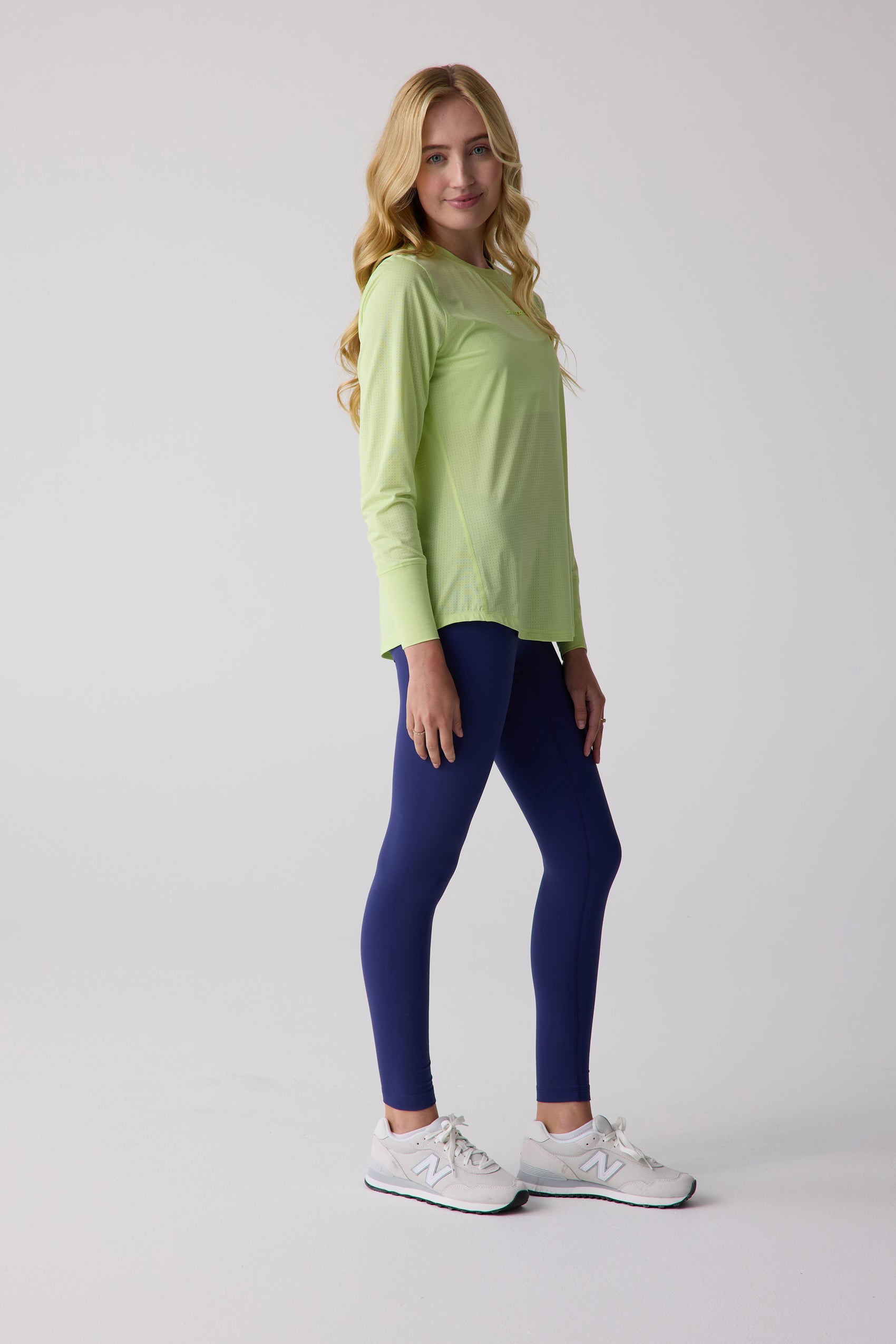 Lime green AirLite women's long sleeve shirt by Centerline Athletics, with perforated texture, worn with navy leggings and white sneakers.