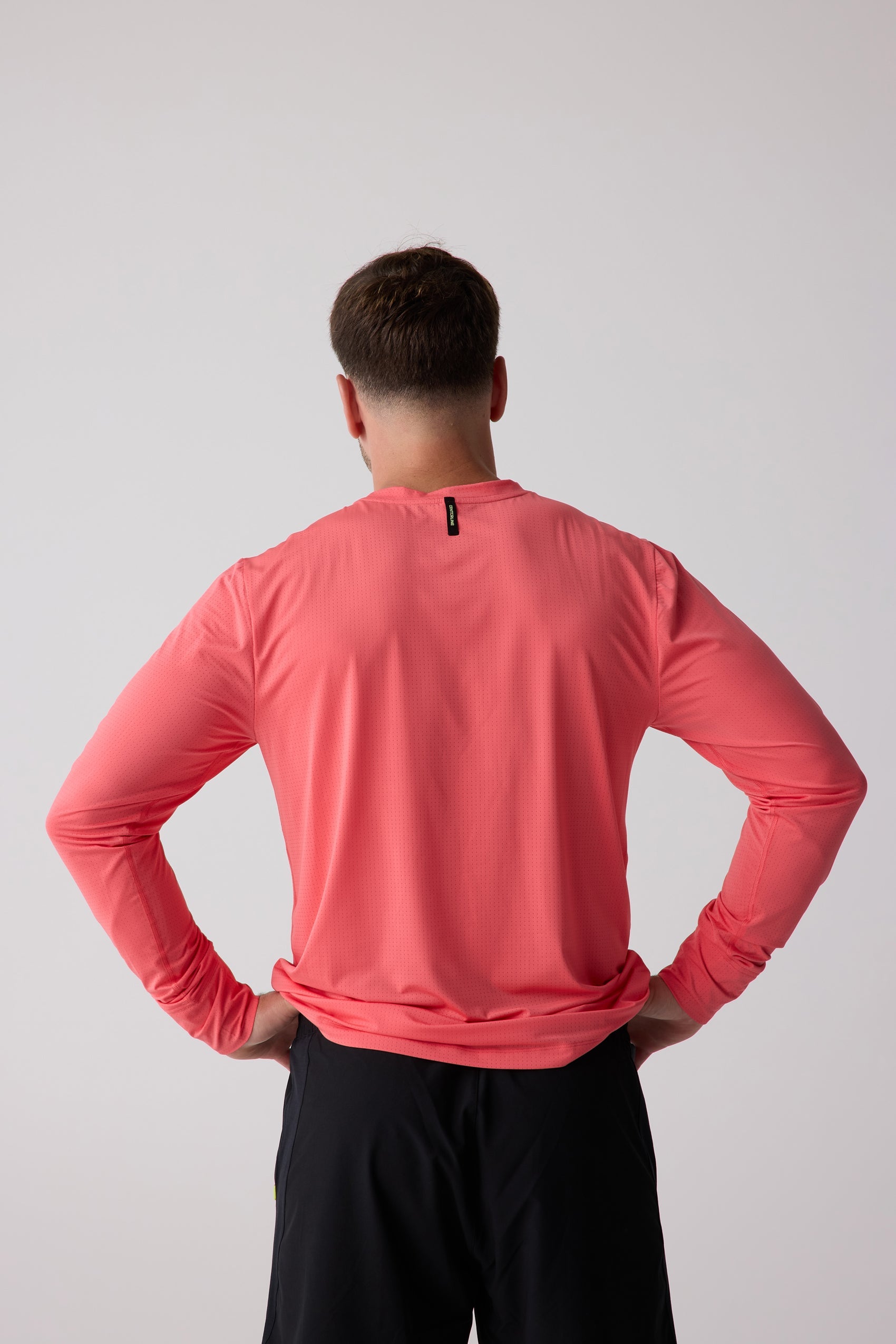 Coral men's long sleeve shirt by Centerline Athletics, back view, with perforated fabric and a black Centerline tag, worn with black shorts.