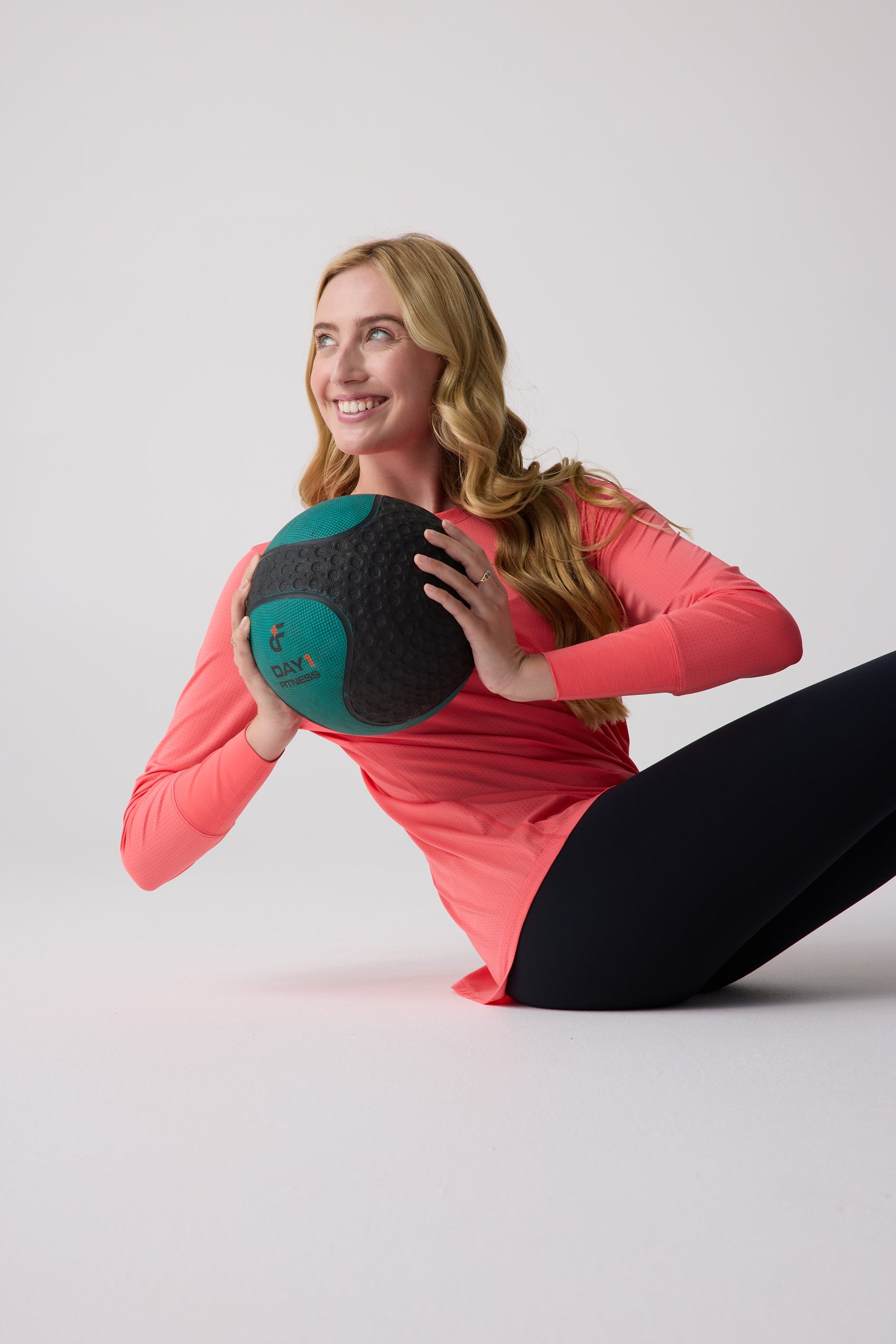 Coral Women's AirLite Long Sleeve Shirt by Centerline Athletics, with perforated fabric, worn by a smiling woman holding a medicine ball.