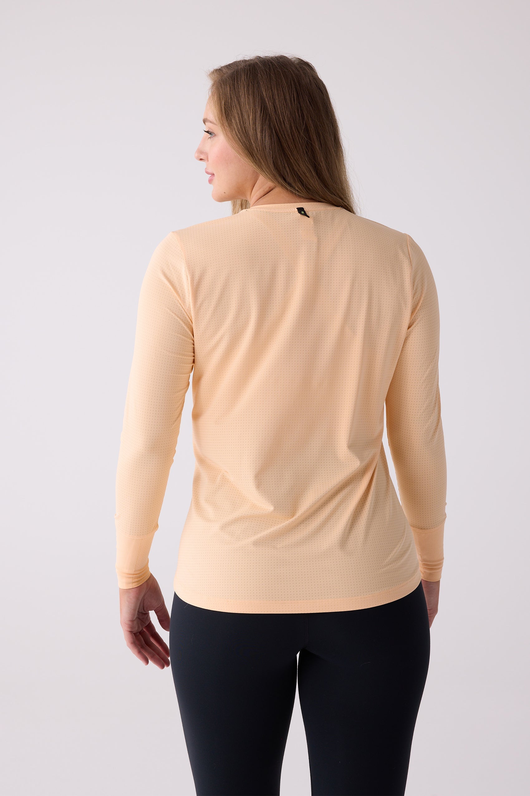 Light peach micro-perforated long sleeve shirt by Centerline Athletics, shown from the back with a black neck tag and black leggings.