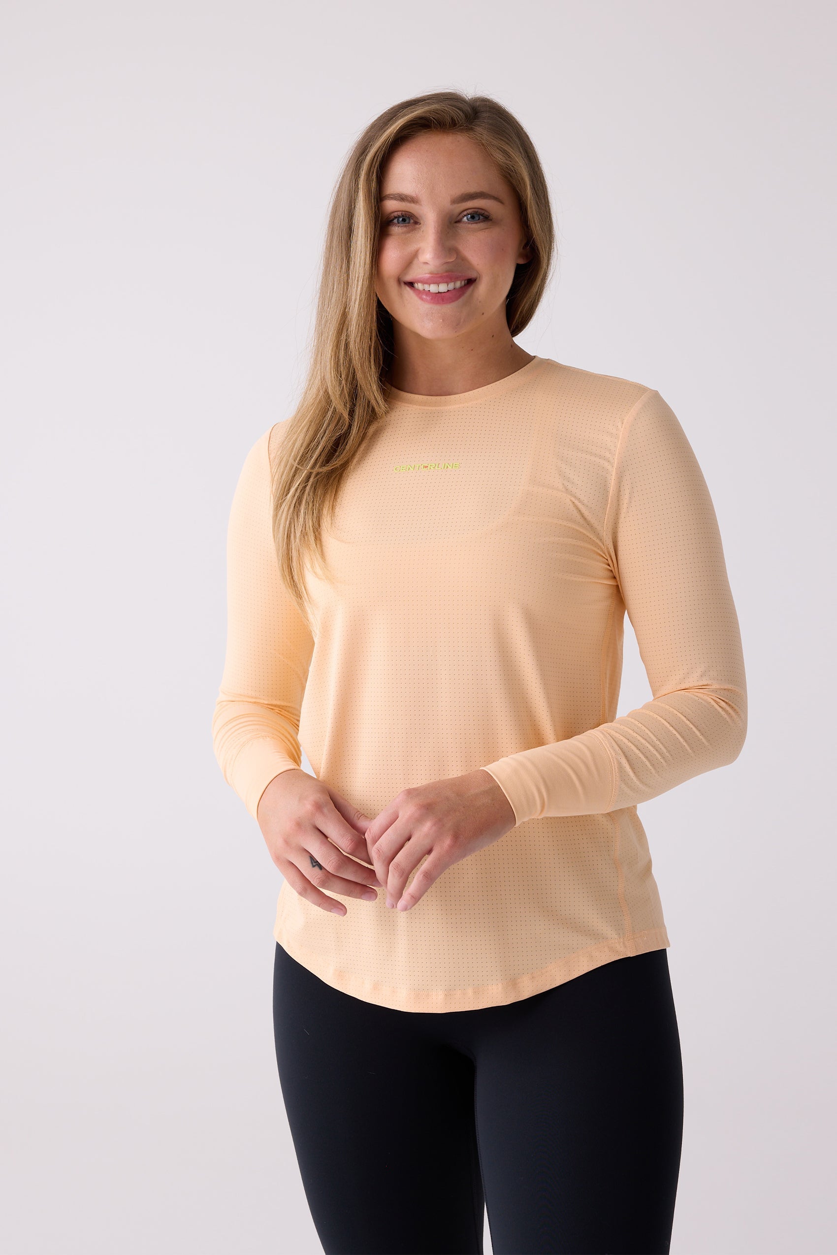 Peach long sleeve shirt by Centerline Athletics, featuring a subtle perforated texture and lime green logo, worn with black leggings.