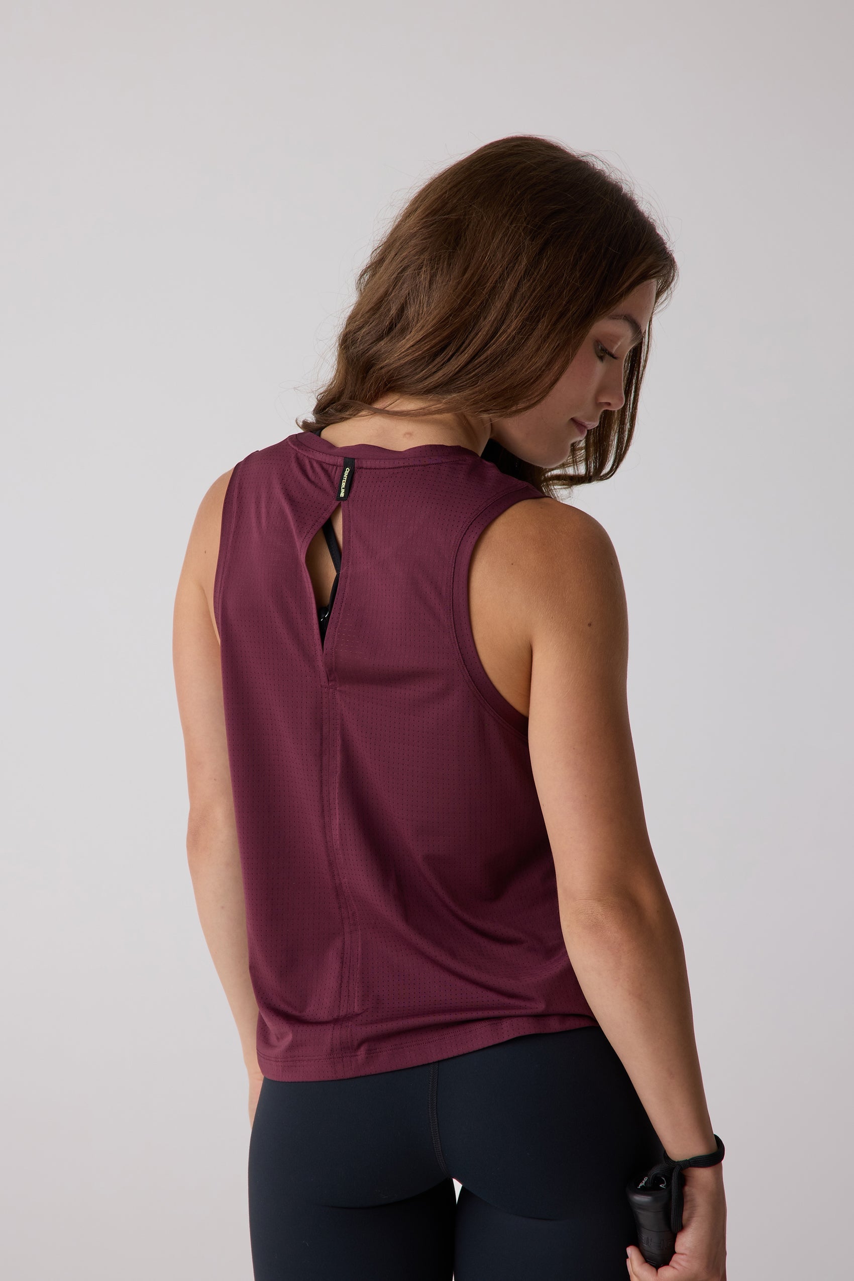 Burgundy perforated tank top by Centerline Athletics, back view with a keyhole cutout, styled with black leggings and a jump rope.