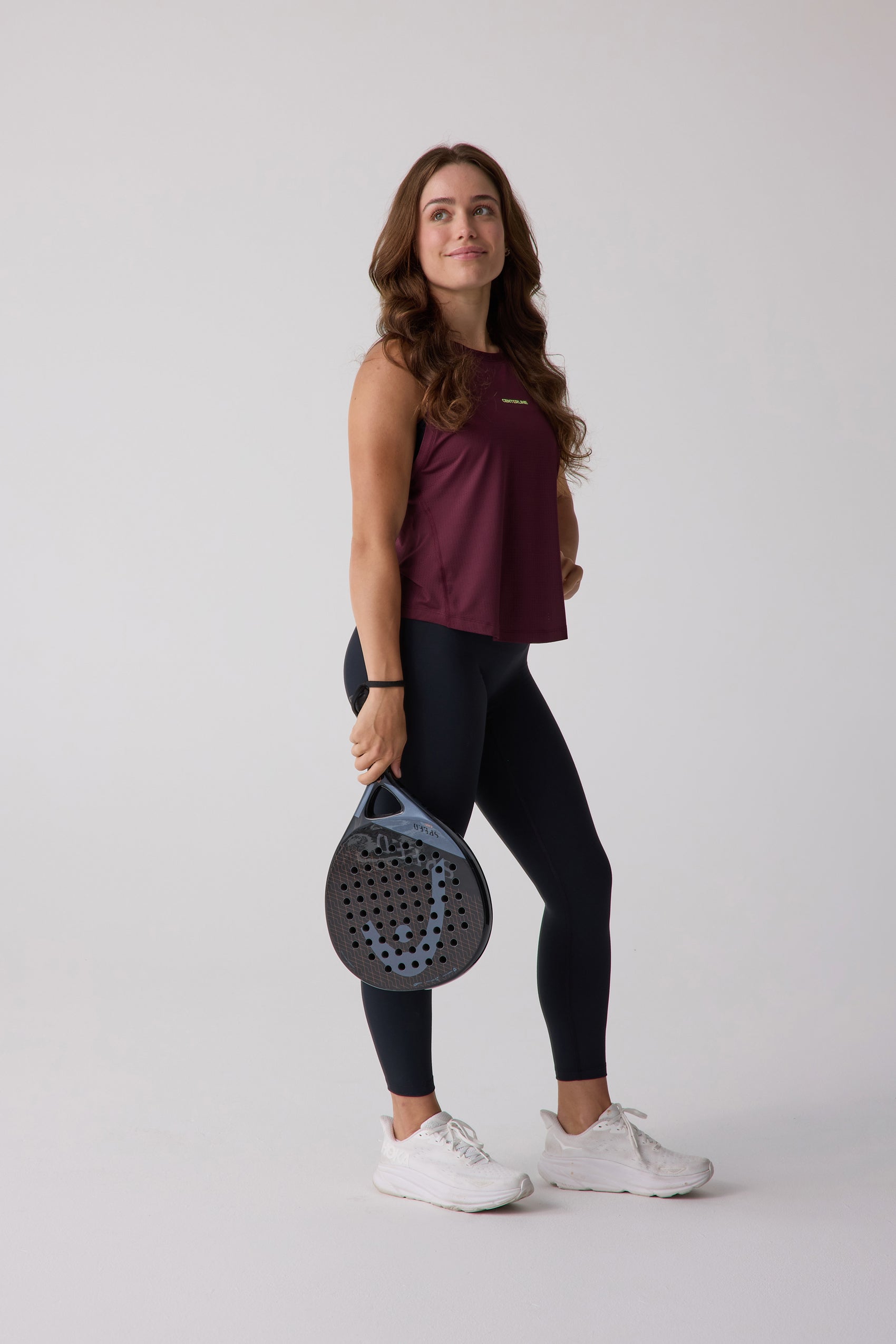 Maroon AirLite Tank by Centerline Athletics, a textured sleeveless top worn with black leggings and white sneakers, holding a paddle racket.