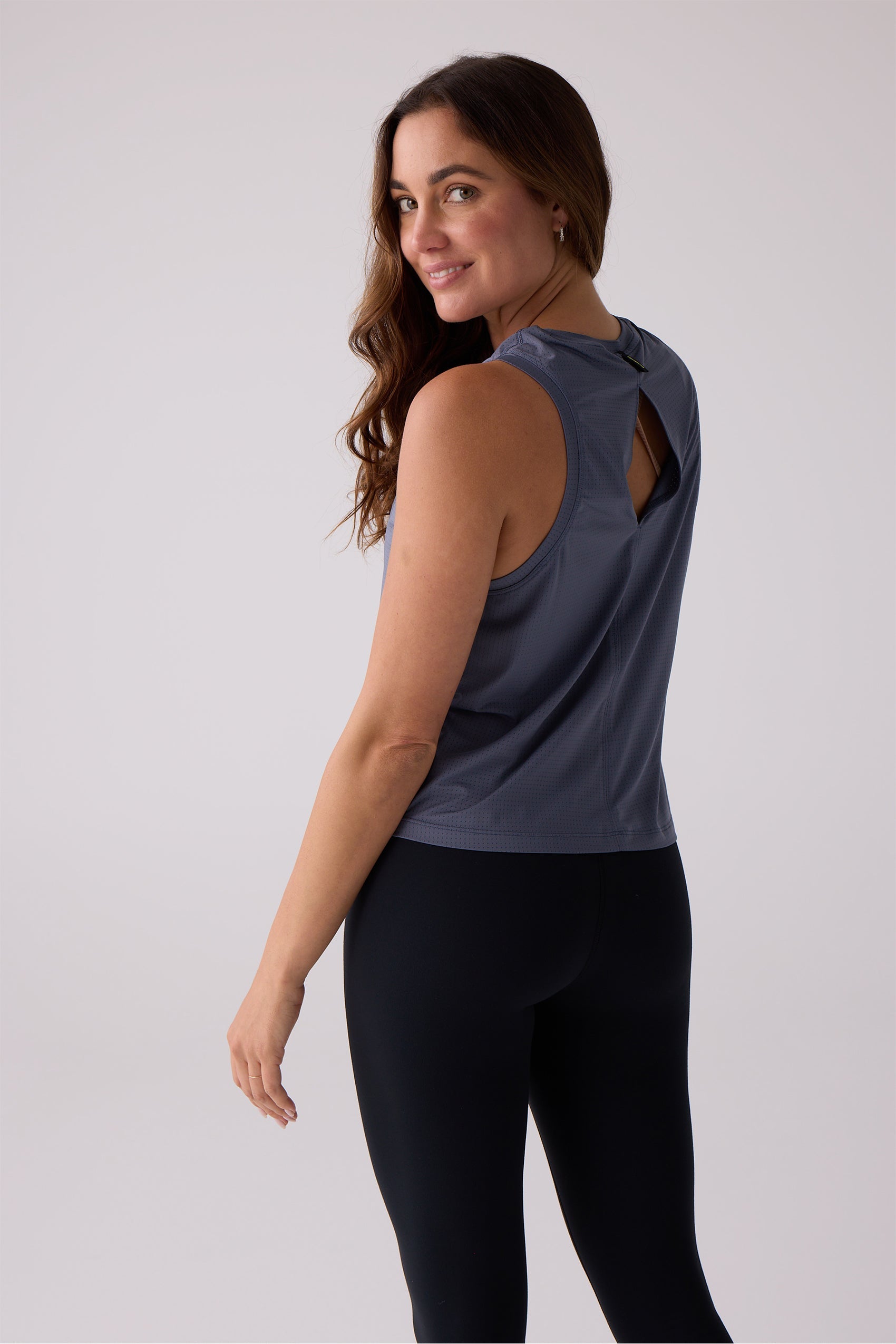 Dark blue-grey perforated tank by Centerline Athletics with a back cutout, worn with black leggings.