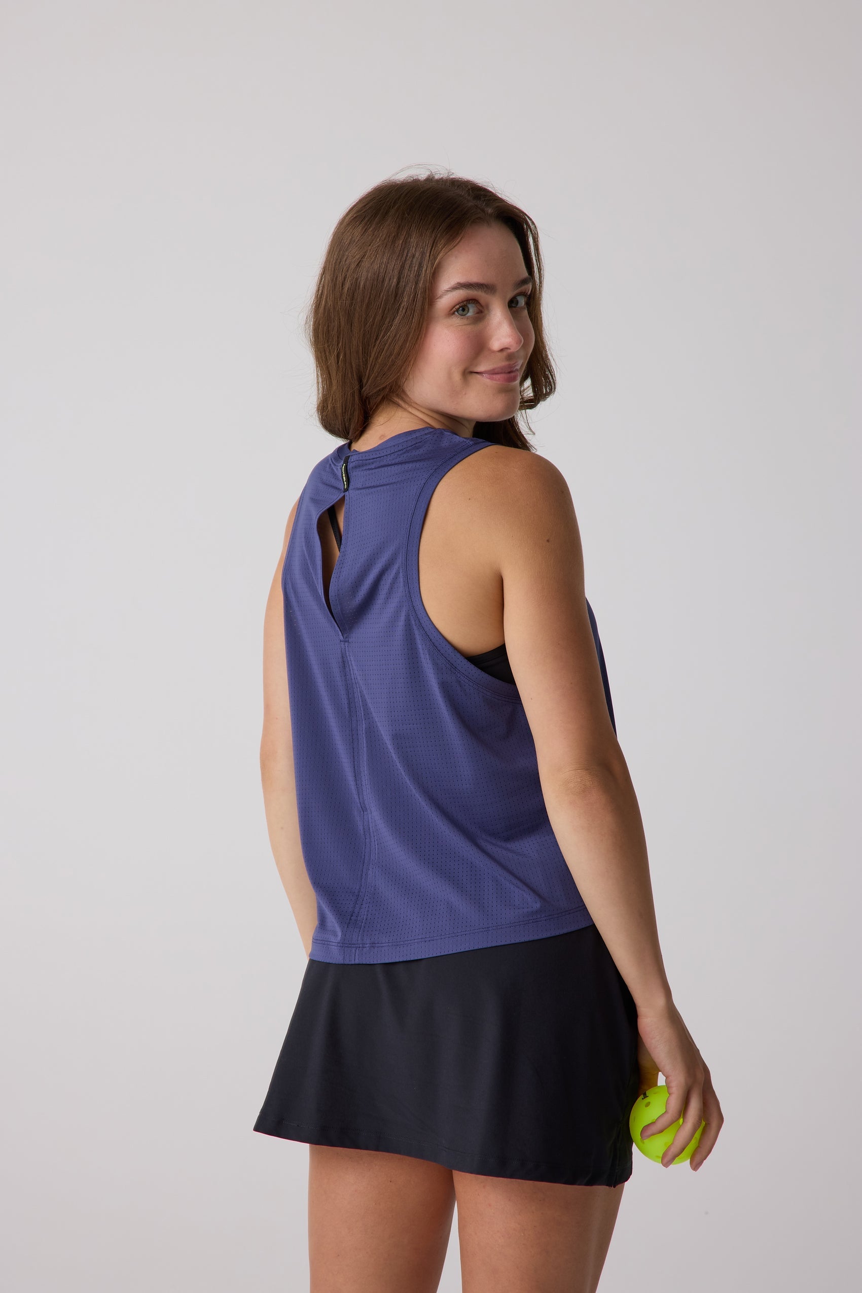 Deep lavender perforated Women's AirLite Tank by Centerline Athletics, featuring a keyhole back, worn with a black tennis skirt and holding a yellow ball.