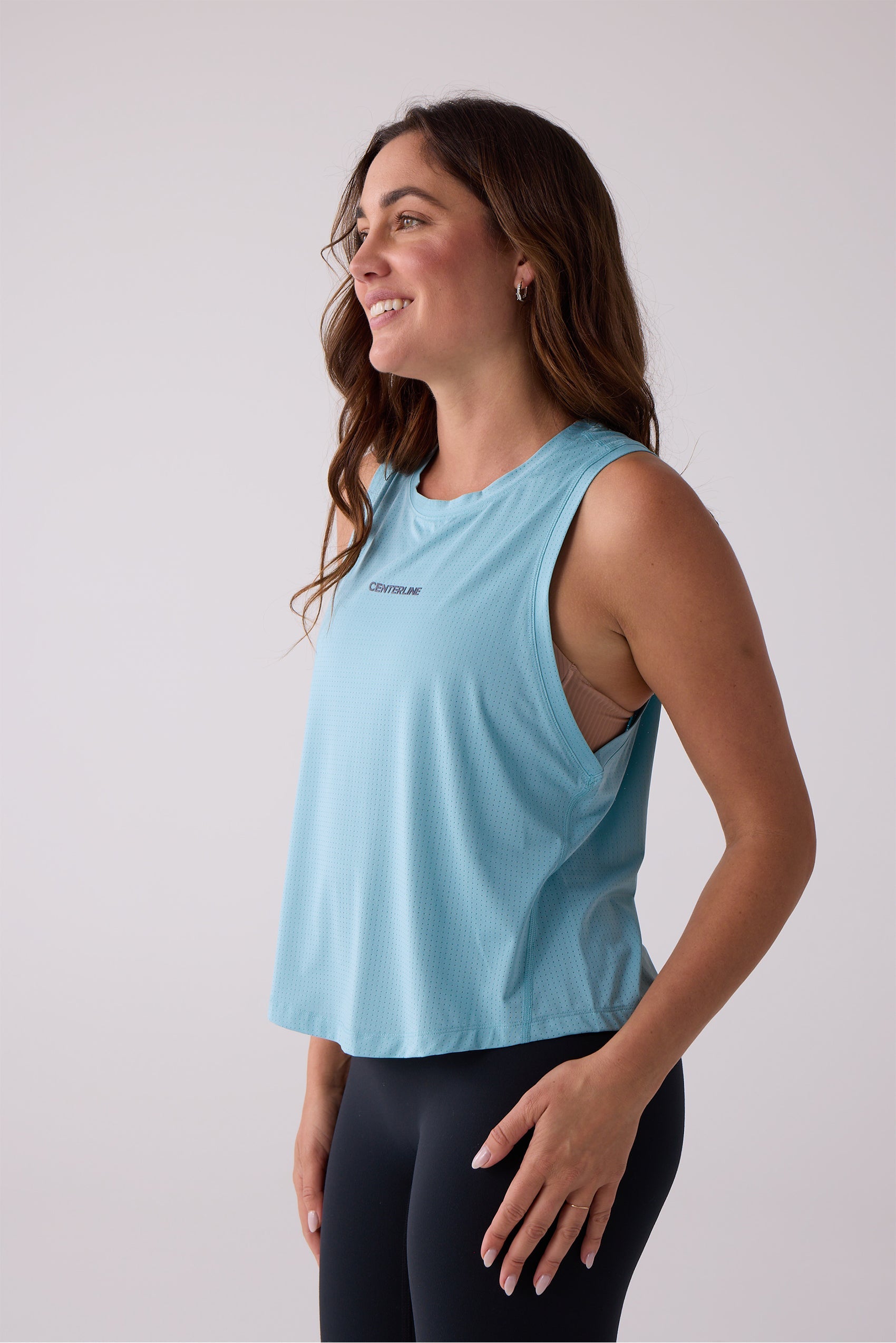 Light blue perforated Women's AirLite Tank by Centerline Athletics, featuring "CENTERLINE" text on the chest, worn by a smiling model.