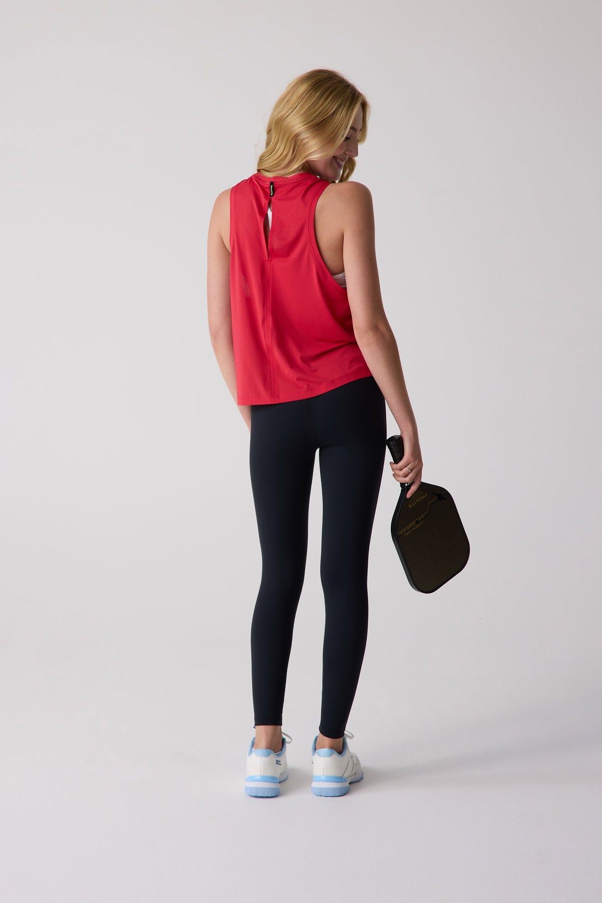 Red mesh women's tank top with back keyhole detail, worn by model in black leggings and white sneakers, holding paddle, back view