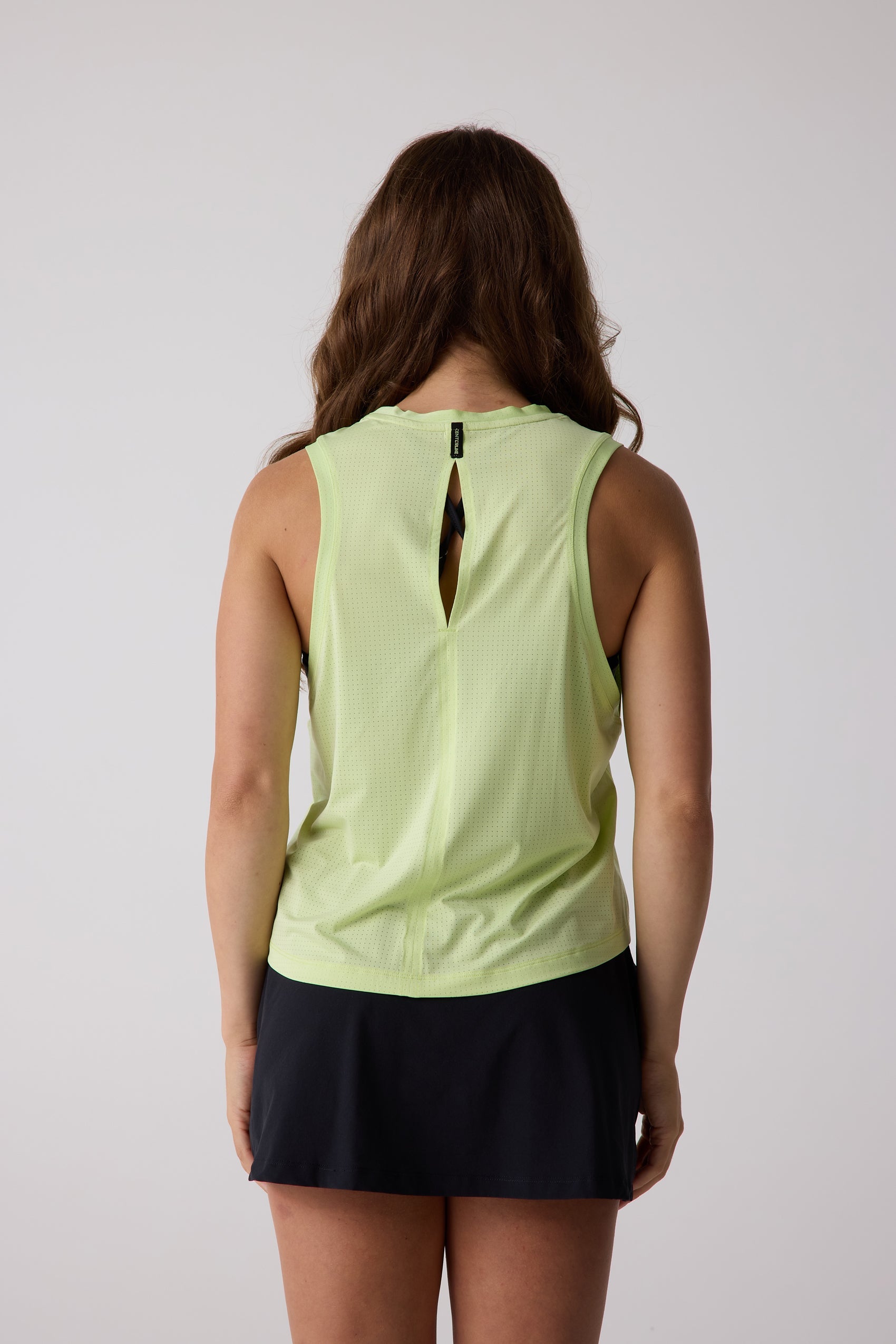 Lime green AirLite tank top by Centerline Athletics, featuring a perforated texture, keyhole back, and brand logo at the neckline, worn by a model in a black skirt.