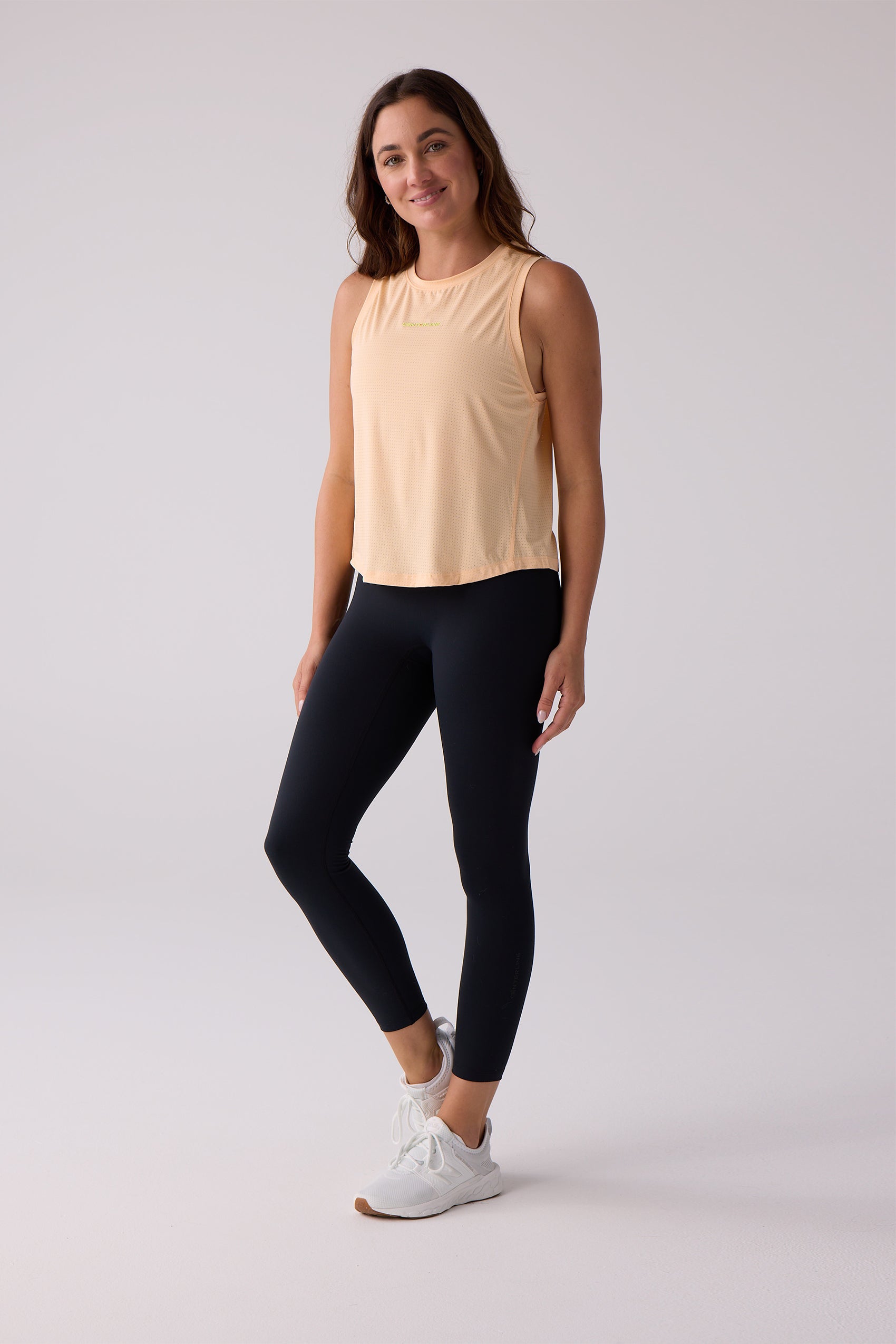 Light orange women's sleeveless tank top by Centerline Athletics, with a perforated texture, paired with black leggings and white sneakers.