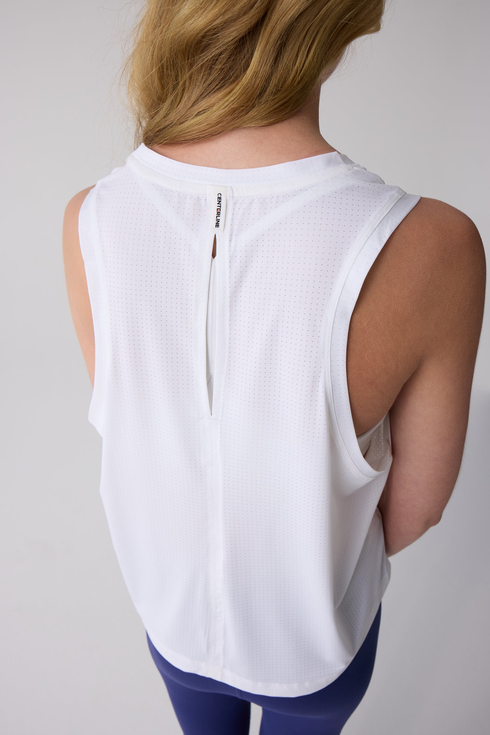 White women's tank by Centerline Athletics, featuring perforated fabric, a round neck, and a keyhole cutout on the back with "CENTERLINE" text.