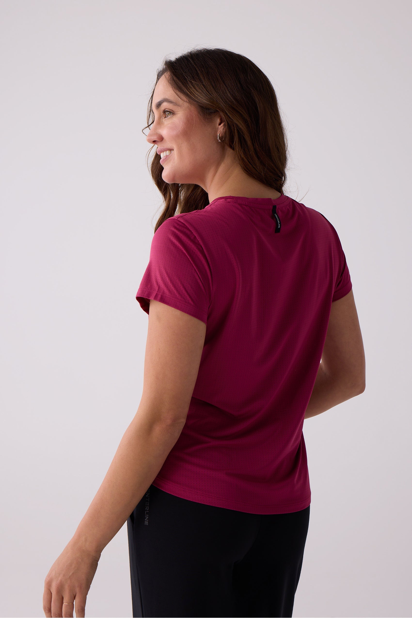 Magenta perforated short sleeve tee by Centerline Athletics with a black brand tag at the back of the neck, shown on a model from a side and back view.