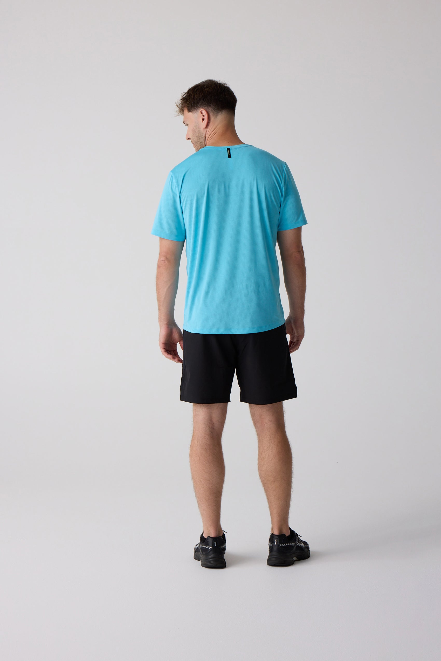 Men's teal AirLite tee by Centerline Athletics, textured, with small black neck label, rear view on man in black shorts and shoes.