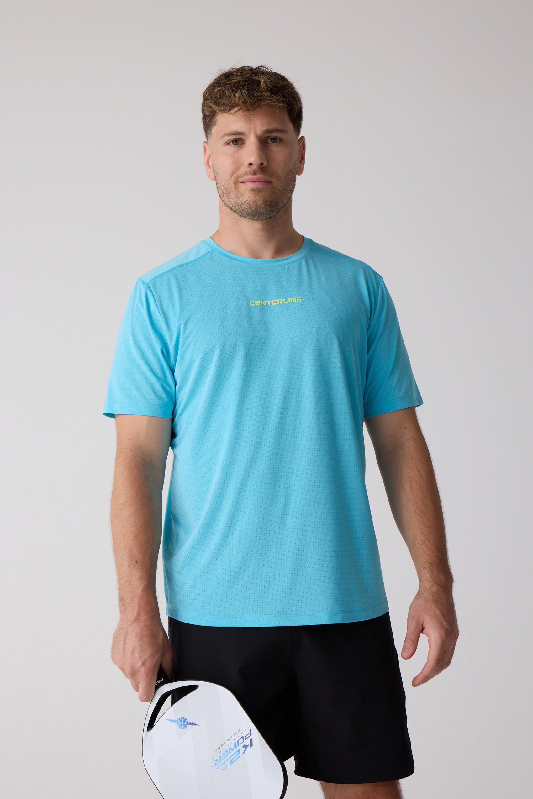 Light blue Men's AirLite Tee by Centerline Athletics, with a perforated texture and 'CENTERLINE' logo, worn by a man holding a paddle.