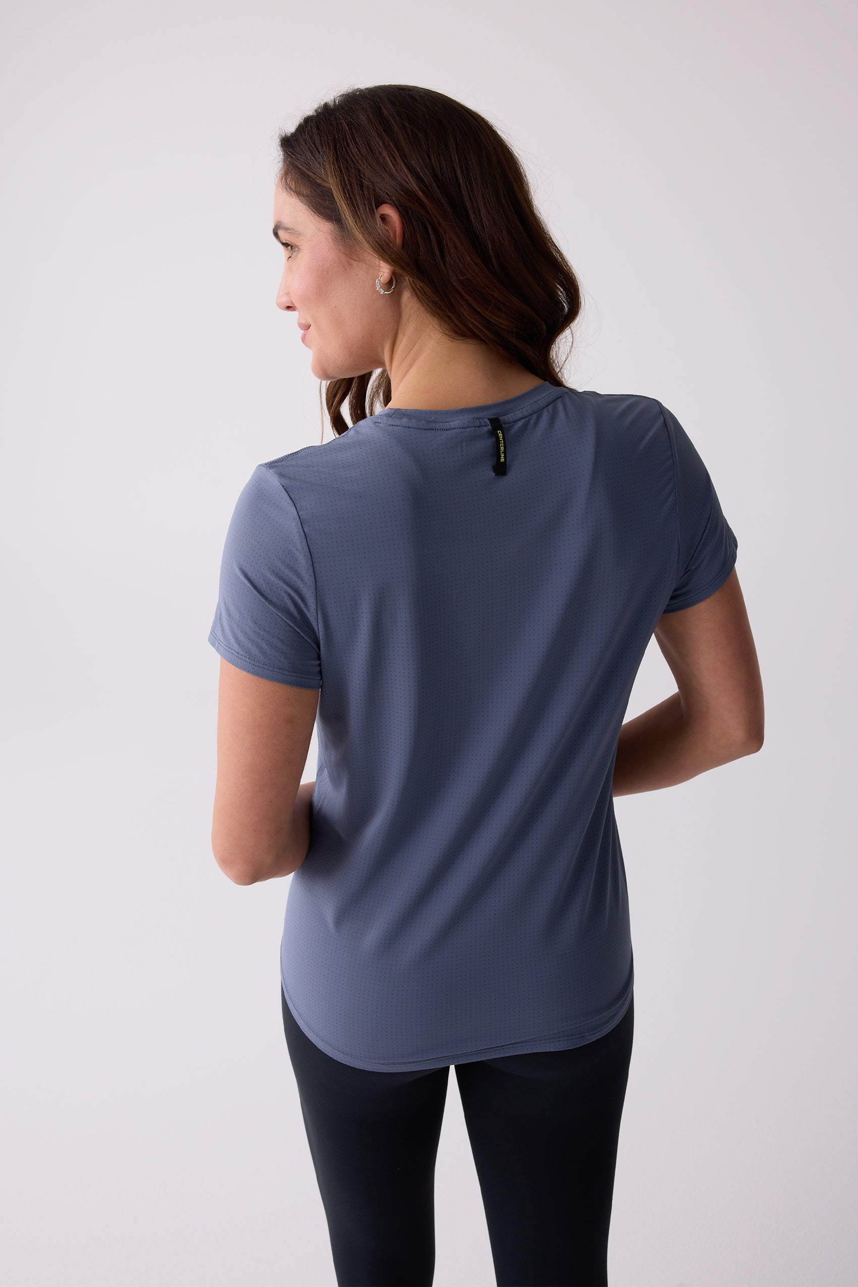Blue micro-perforated women's short sleeve tee by Centerline Athletics, with a brand tag on the back, worn with black leggings.