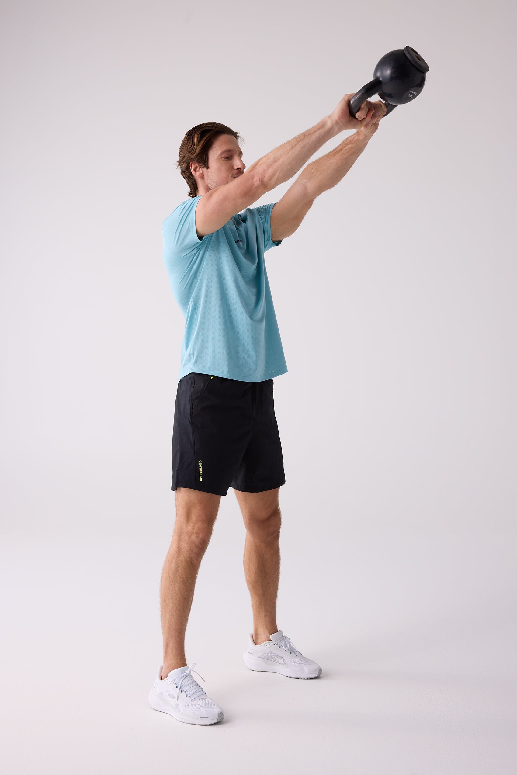 Light blue short-sleeved men's tee shirt by Centerline Athletics, subtly textured, worn by a man doing a kettlebell swing.
