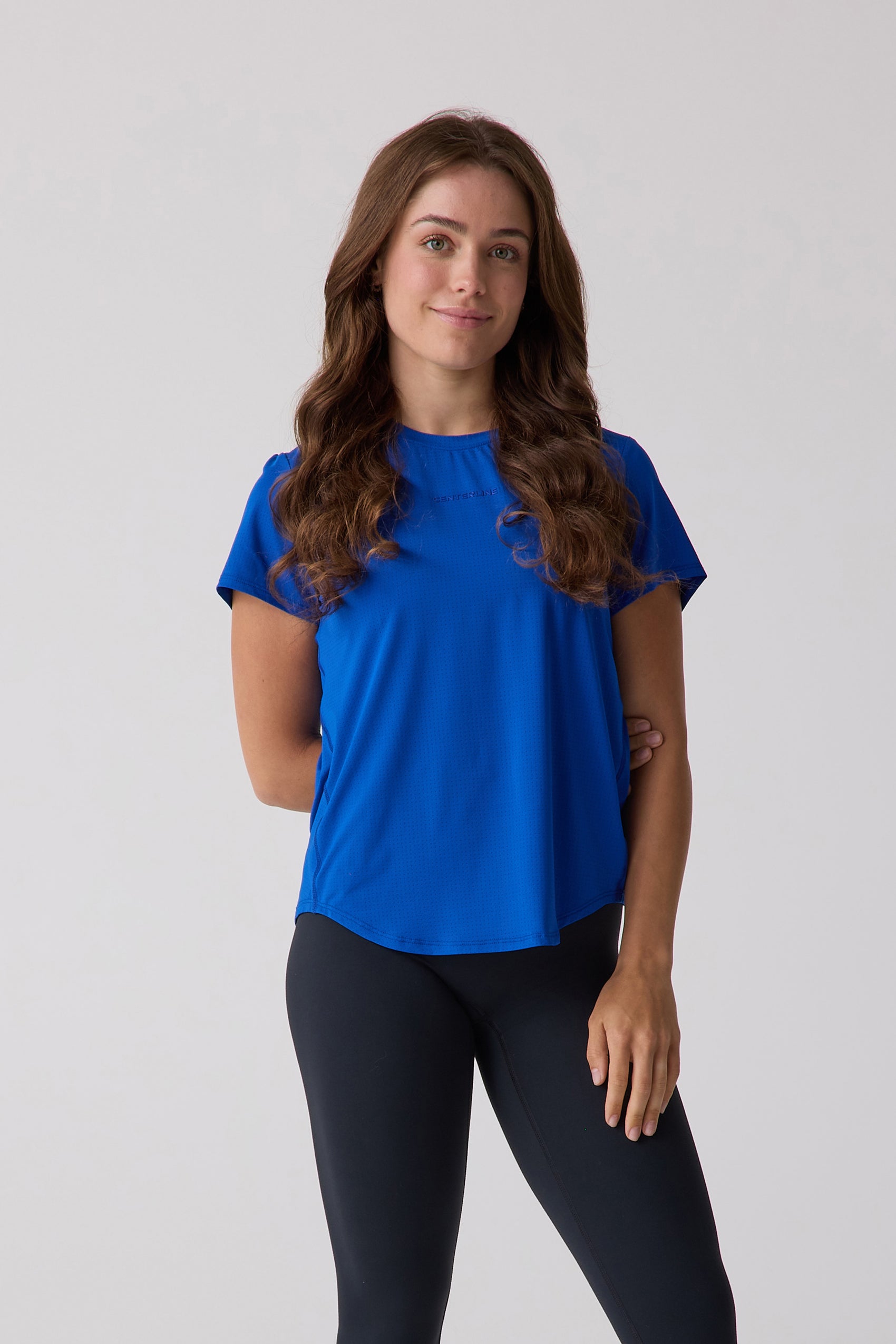 Royal blue women's short sleeve tee by Centerline Athletics with a textured knit, embossed logo, and rounded hem, worn with black leggings.