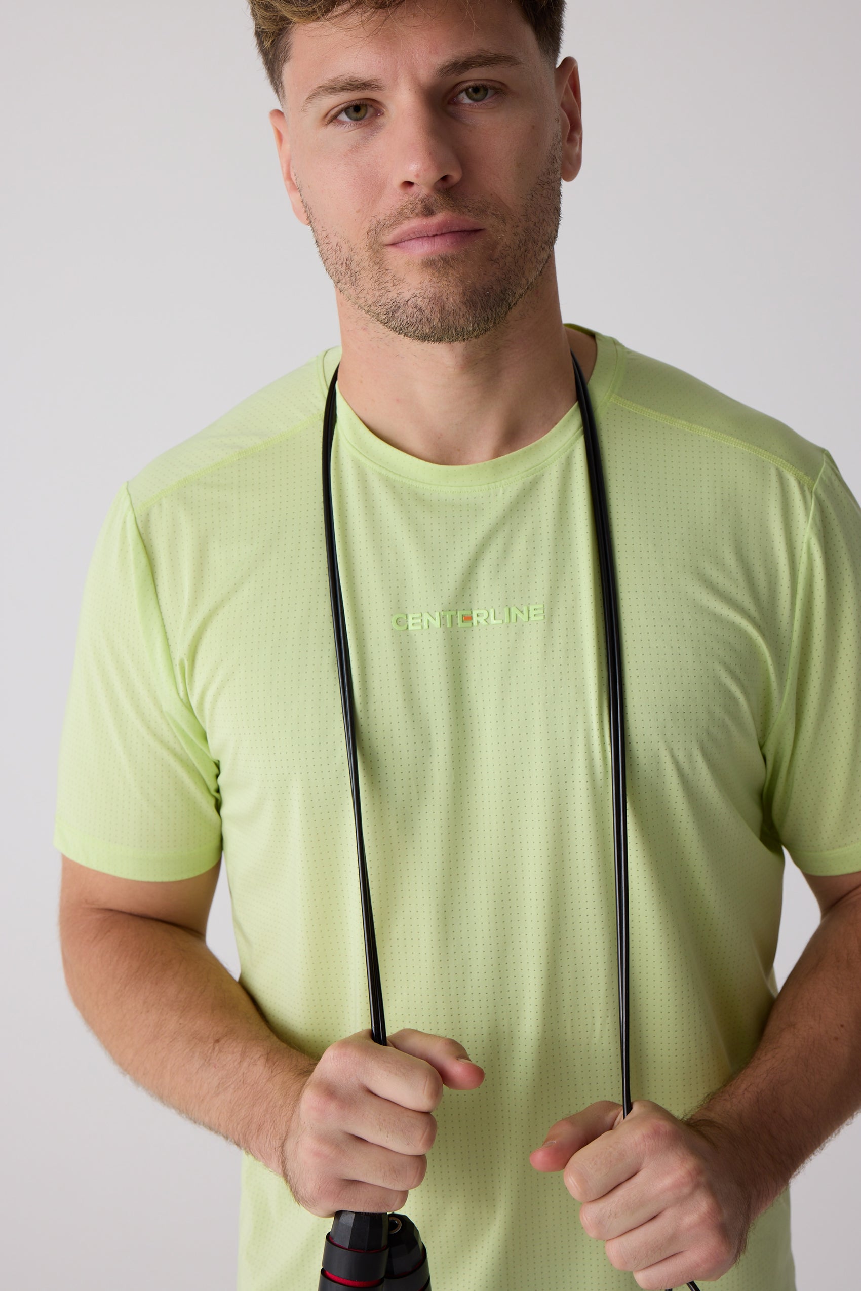Lime green perforated men's short-sleeve tee by Centerline Athletics, with 'CENTERLINE' text on chest, worn by a man holding a jump rope.