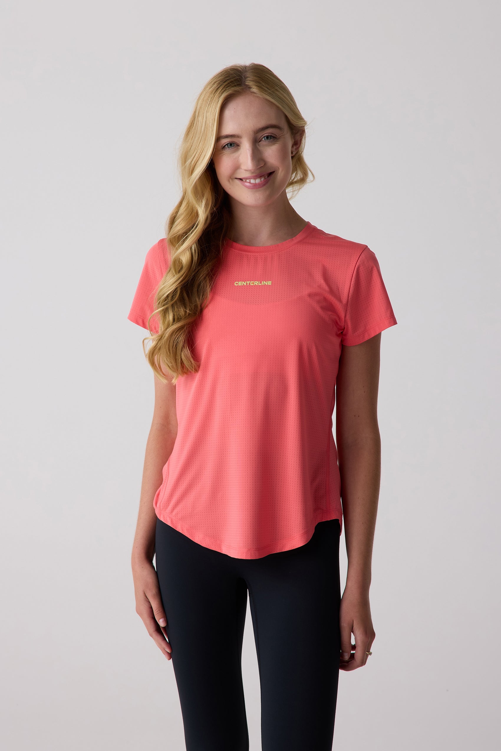 Coral perforated short sleeve shirt by Centerline Athletics with a gold 'CENTERLINE' logo, styled with black leggings.