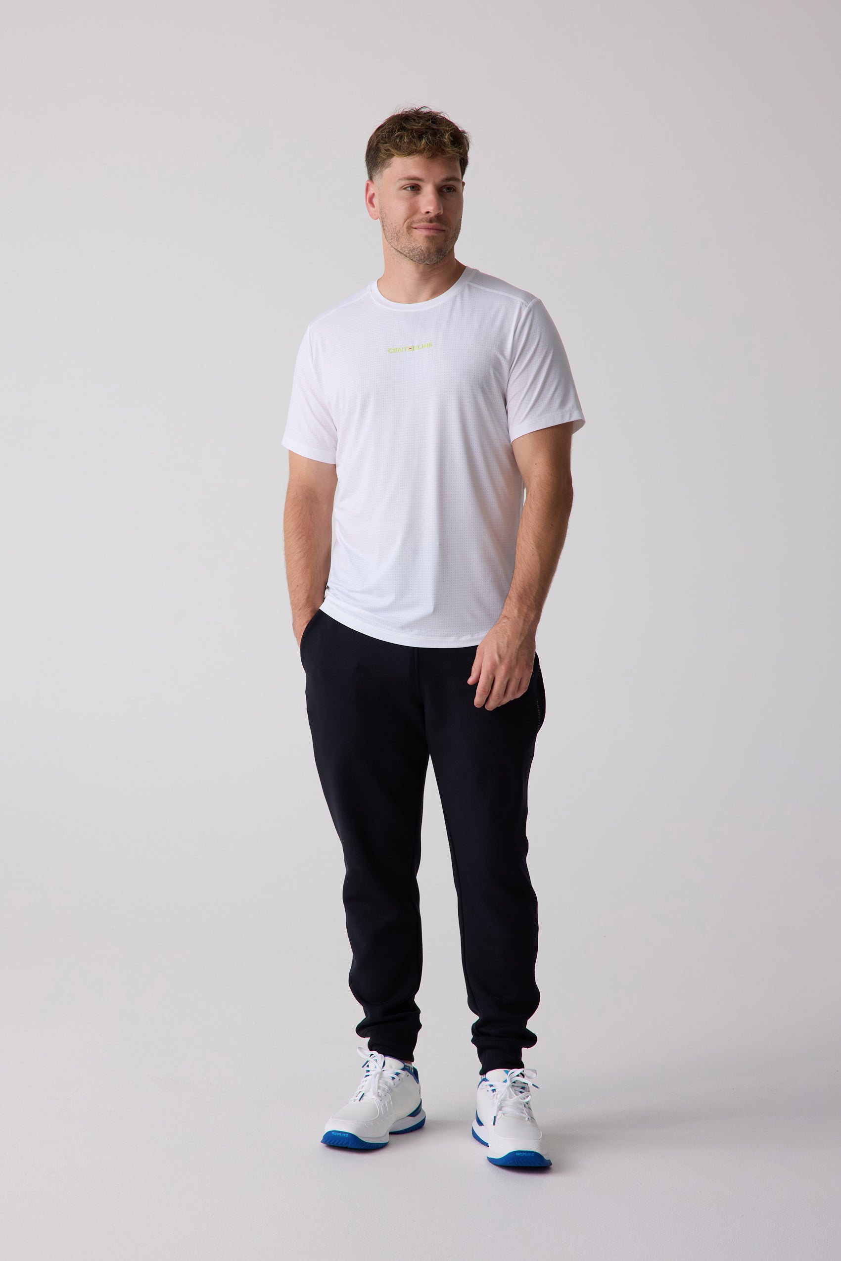White perforated men's AirLite tee by Centerline Athletics, with lime green 'CENTERLINE' text, styled with black joggers and athletic shoes.