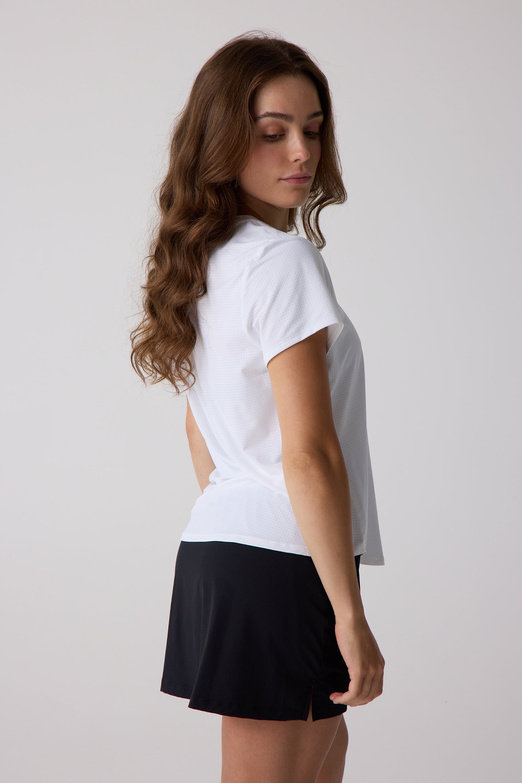 White women's short sleeve shirt by Centerline Athletics, with a subtle perforated texture, paired with black shorts and worn in a side profile.
