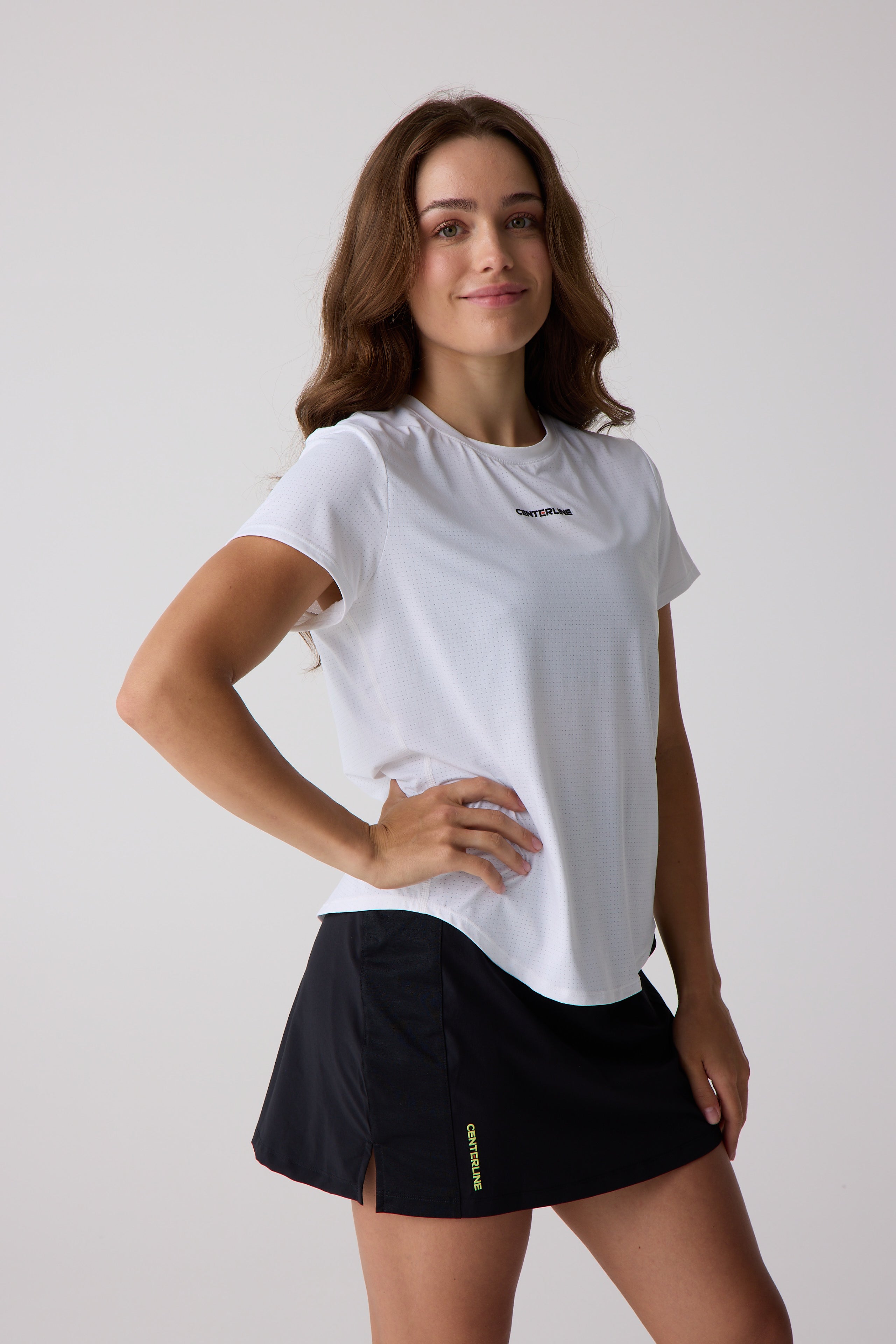 White perforated Women's AirLite Tee by Centerline Athletics with black chest logo, worn with a black skort.