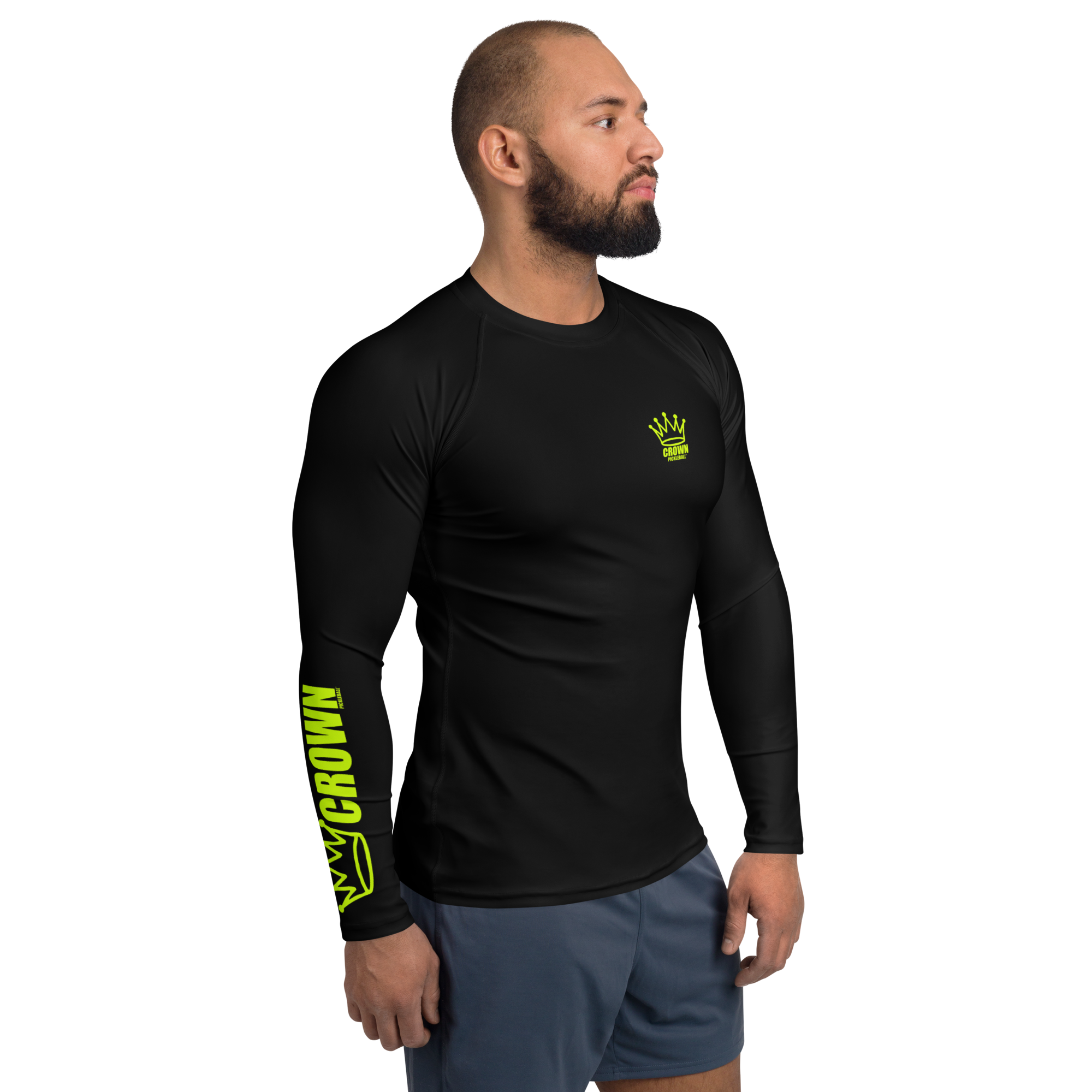 A man wears a black long-sleeved athletic shirt with a green logo and lettering, paired with blue shorts, standing against a black background.