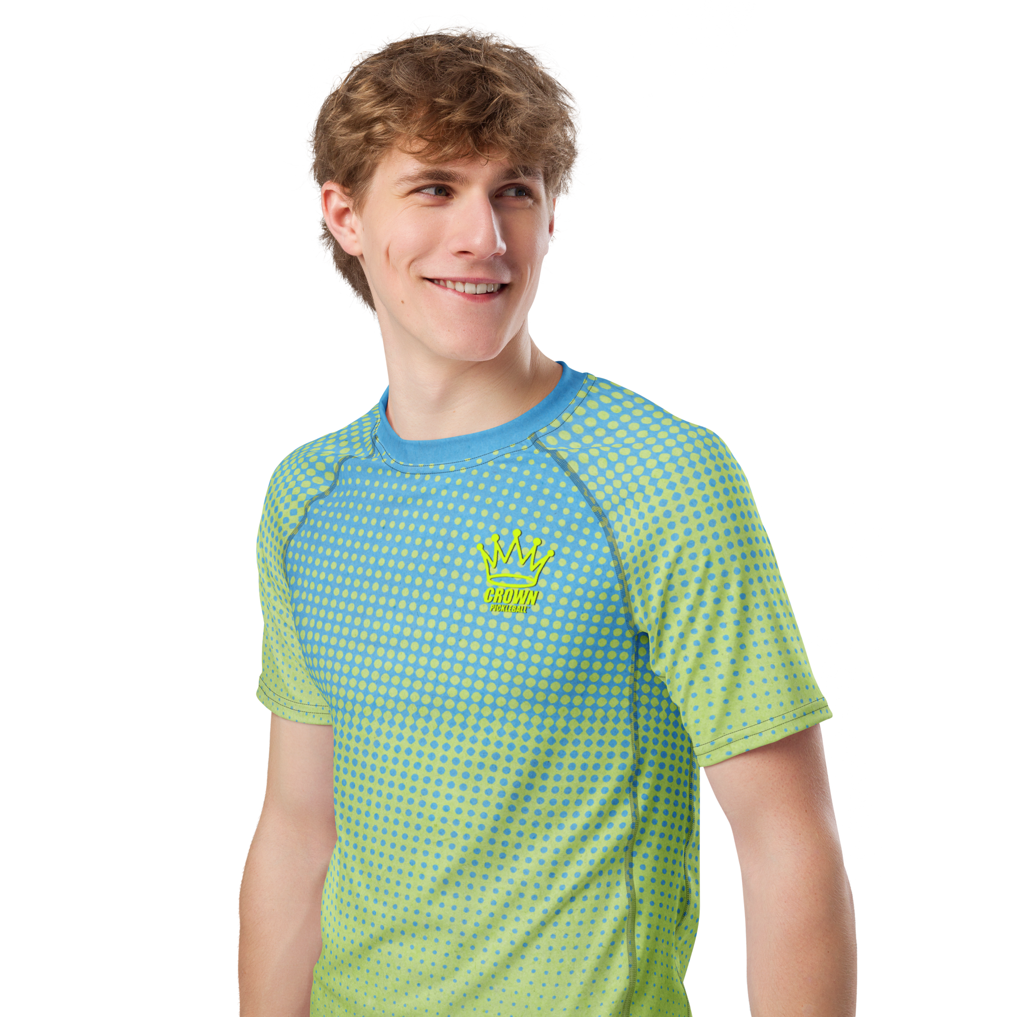 A man in a blue and green patterned t-shirt with a crown logo smiles and looks off to the side against a black background.