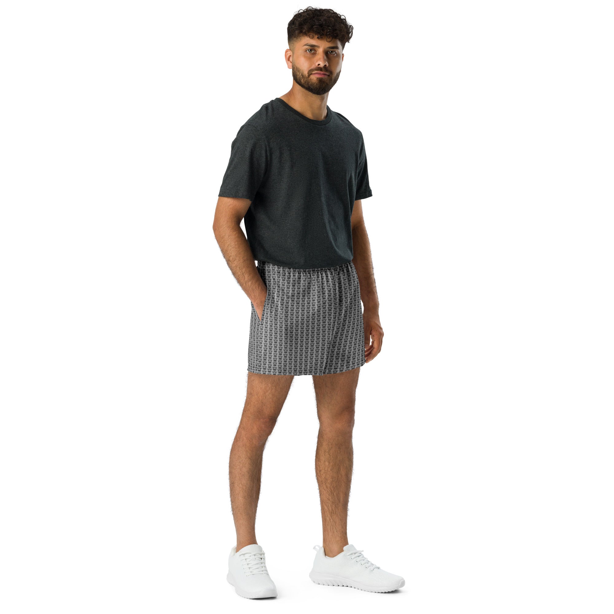 Man in gray t-shirt and crown print shorts standing with hands in pockets.