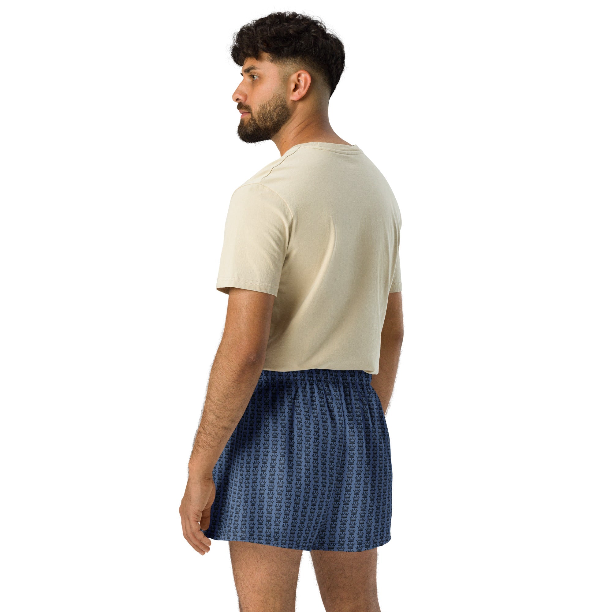 Man in tan t-shirt and blue crown-patterned shorts, looking left.