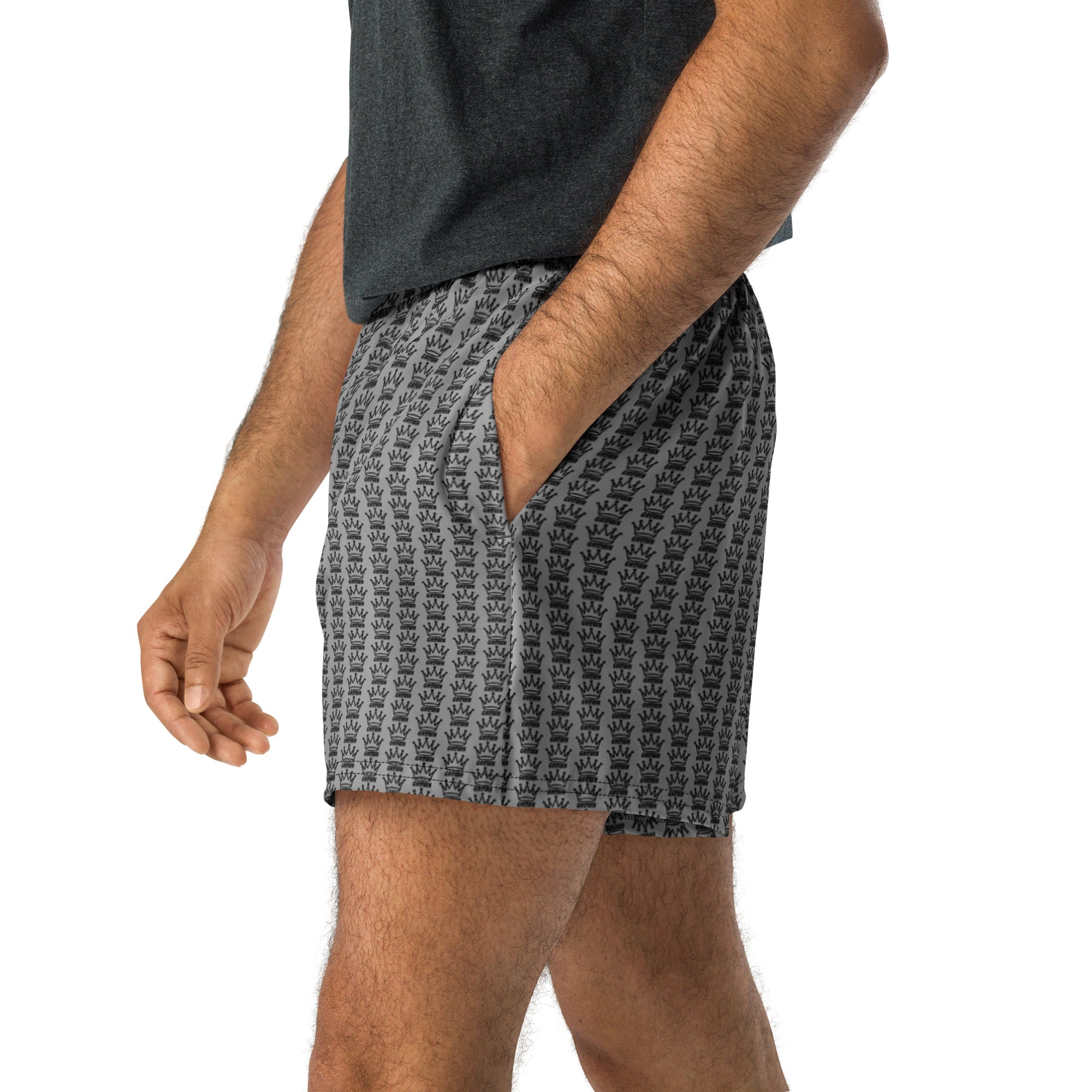 Person wearing gray t-shirt and gray crown-patterned shorts with hand in pocket.