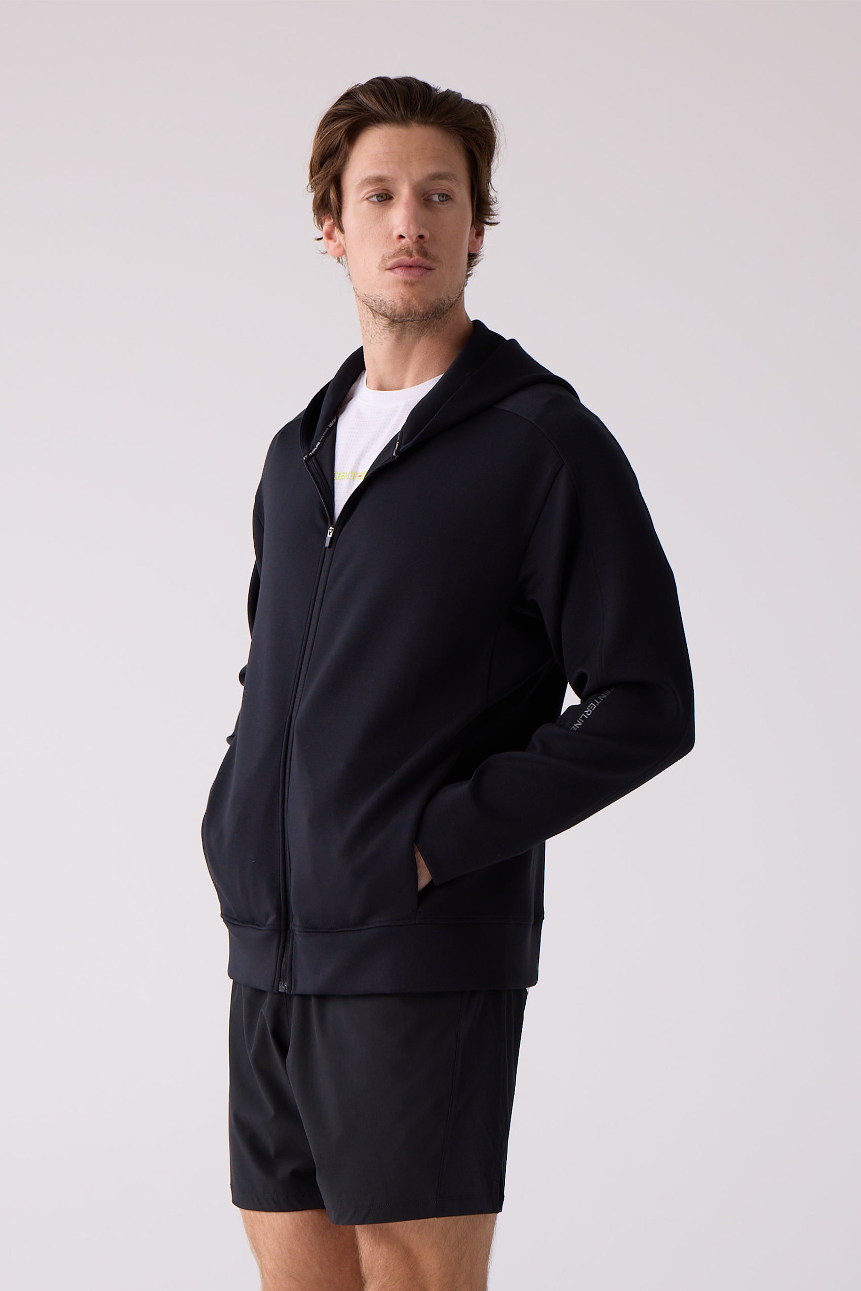 Unisex black full-zip hoodie by Centerline Athletics, with logo text on sleeve, worn by a man in black shorts and a white tee.